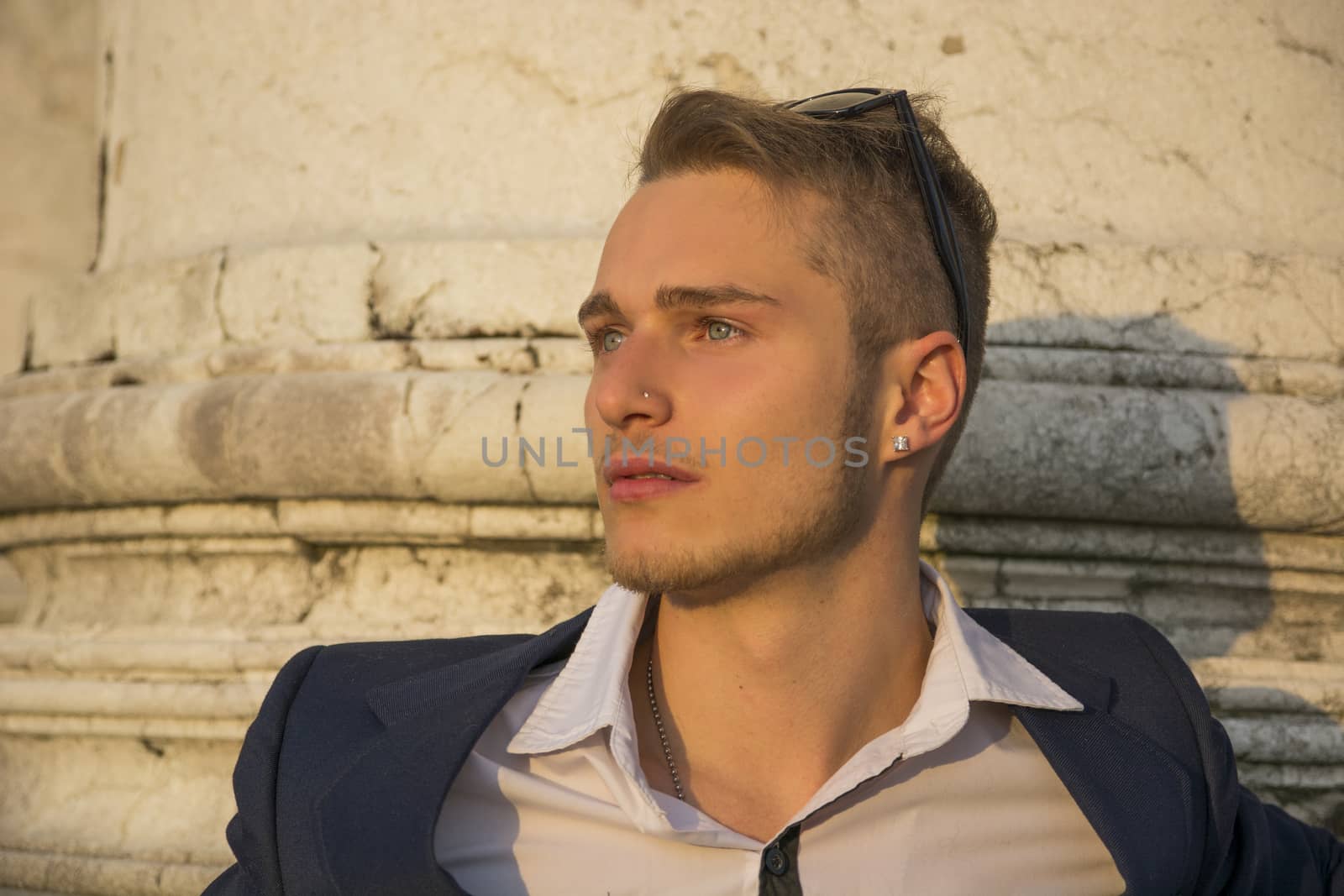 Handsome blond young man with marble columns behind him, looking away