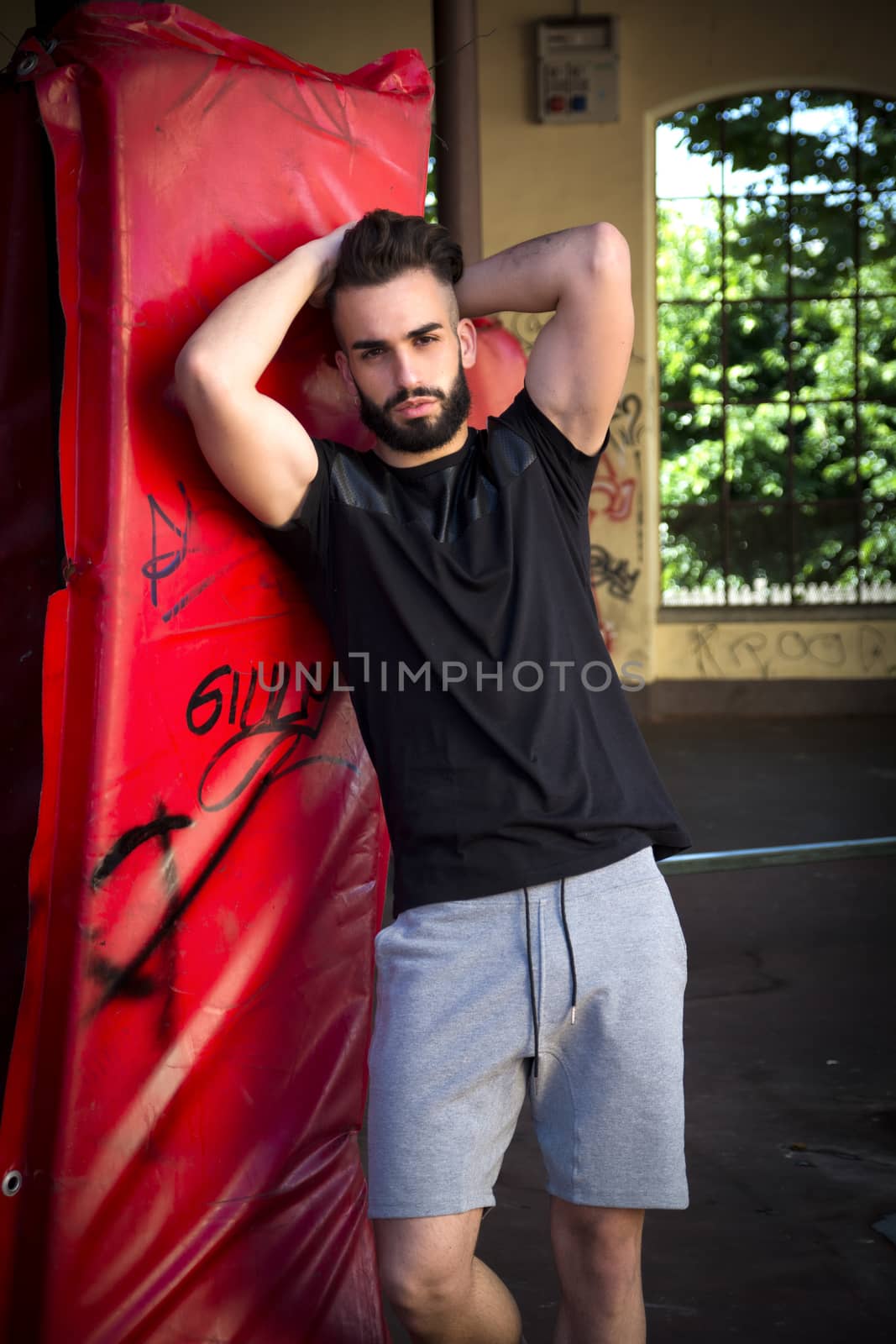 Handsome young man with beard, wearing t-shirt and shorts, standing and looking at camera