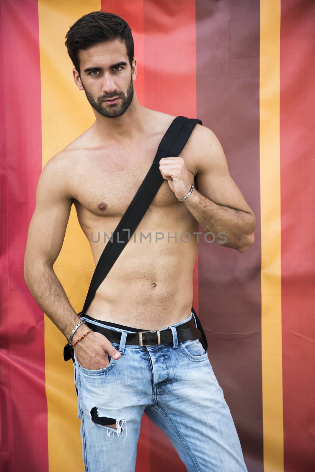 Handsome bearded shirtless young man standing on colorful background, looking at camera