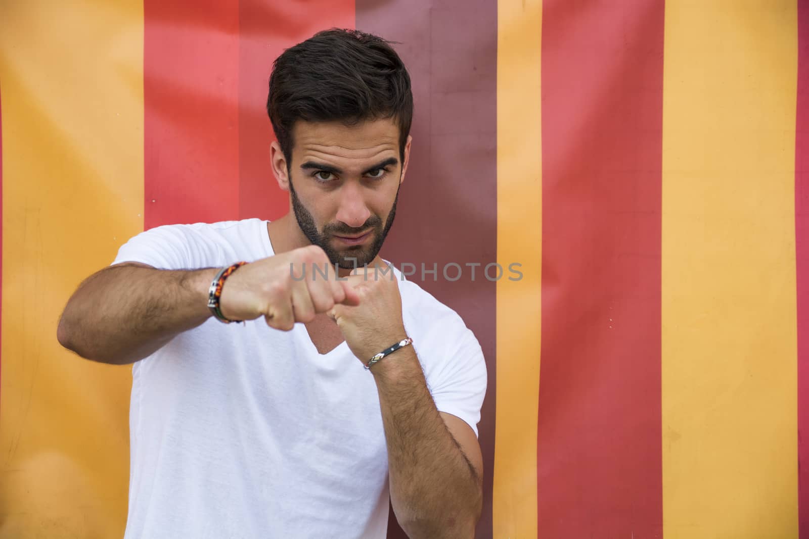 Angry handsome young man throwing punch to camera on colorful background