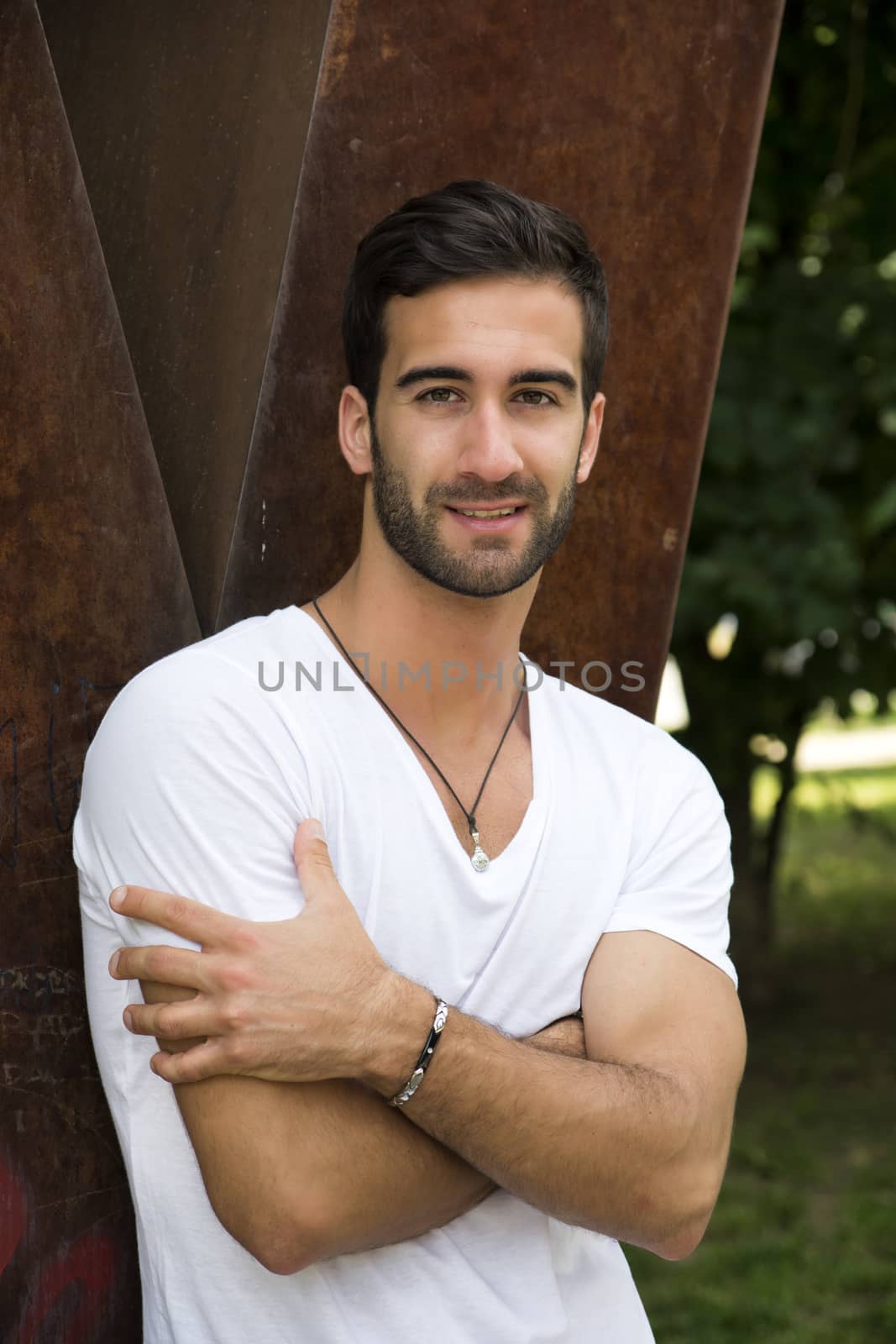 Handsome friendly young man outdoors with arms crossed on chest, smiling at camera