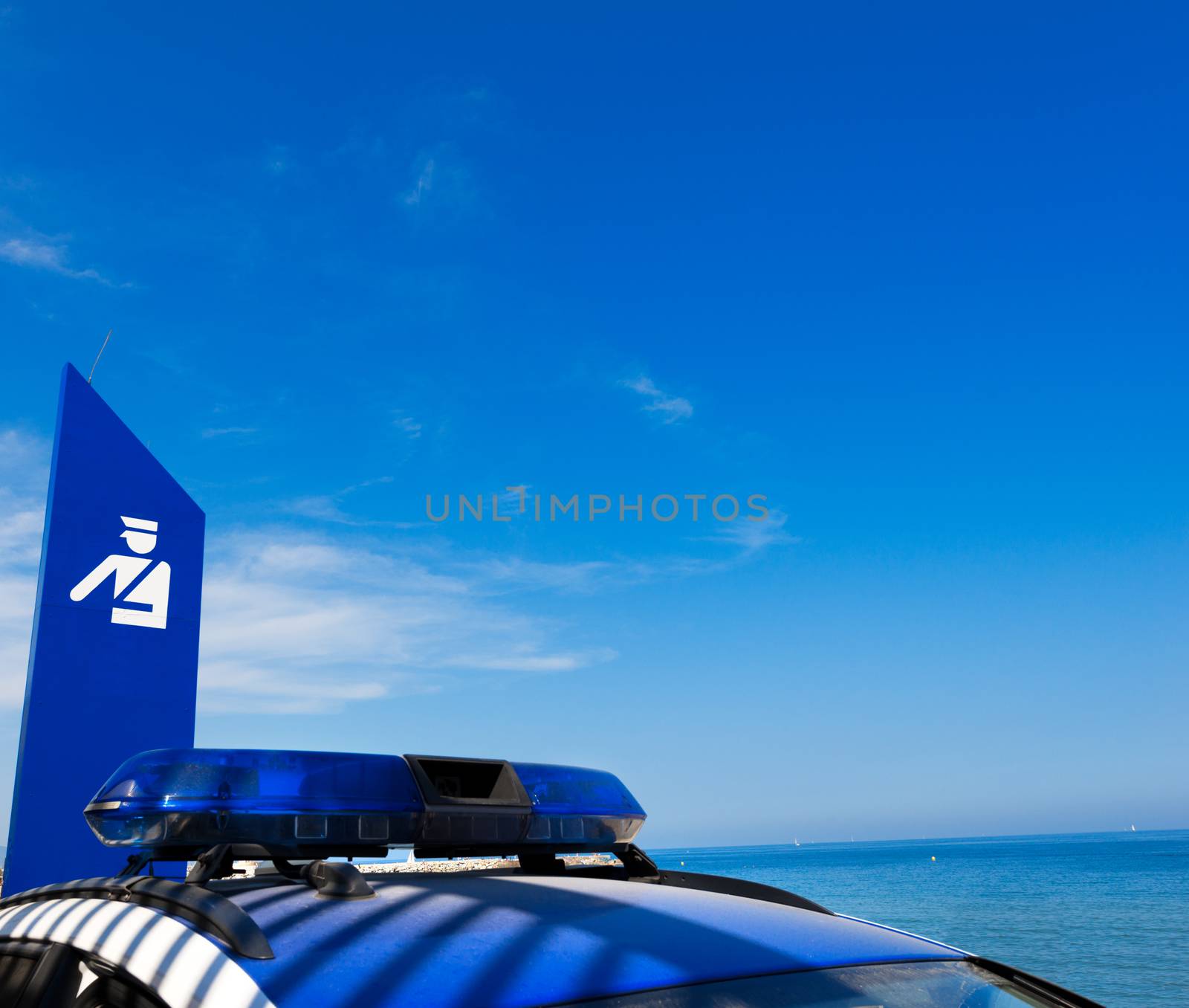 Blue roof lights of a Spanish police car and billboard with symbol of police on sea with blue sky and clouds - Barceloneta beach in Barcelona, Spain