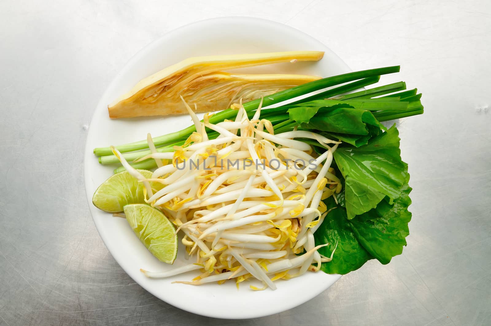 Mix of Thai Vegetable, Bean sprout, lime, banana blossom and Garlic chives on white plate.