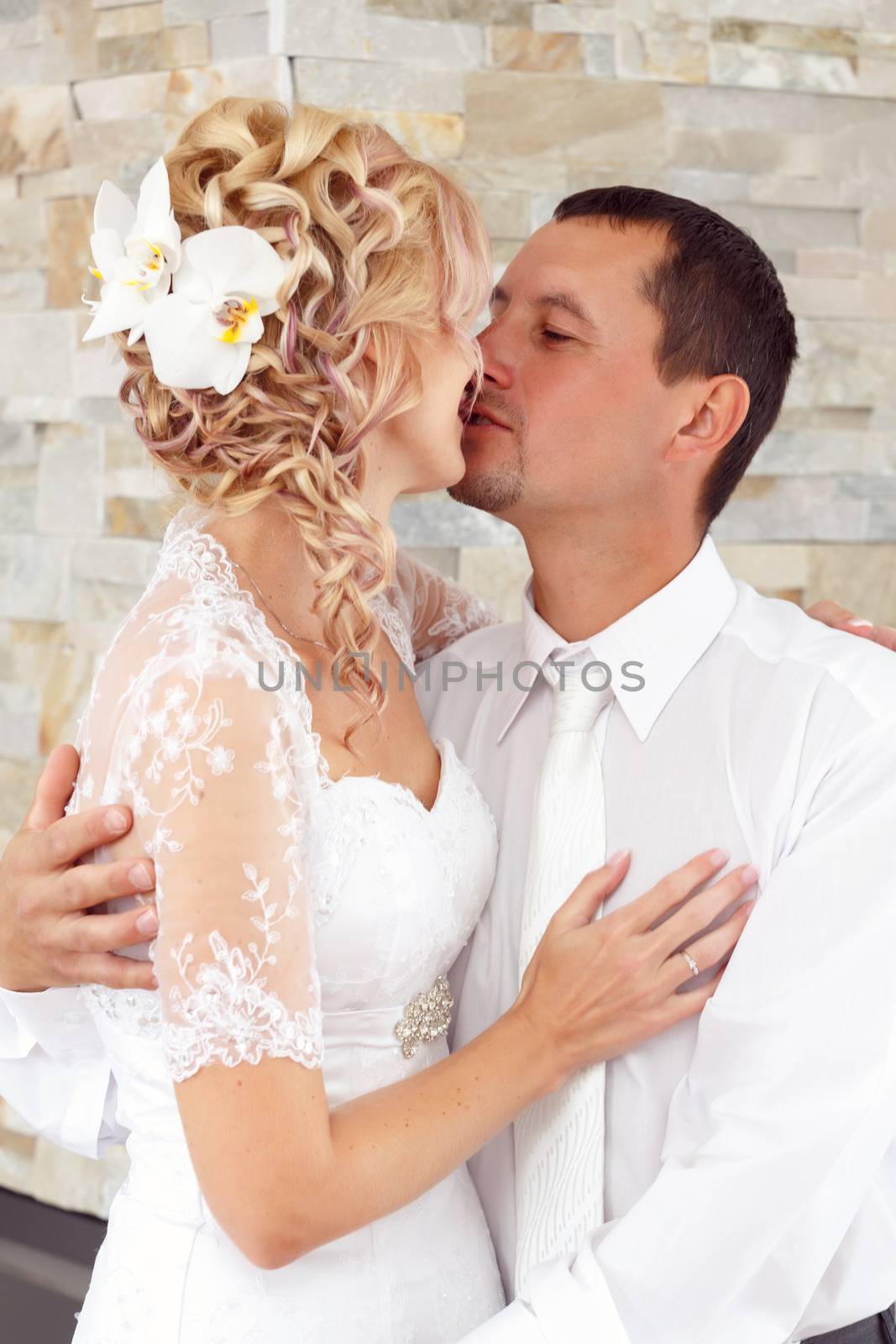 beautiful young wedding couple, blonde bride kissing her groom indoor
