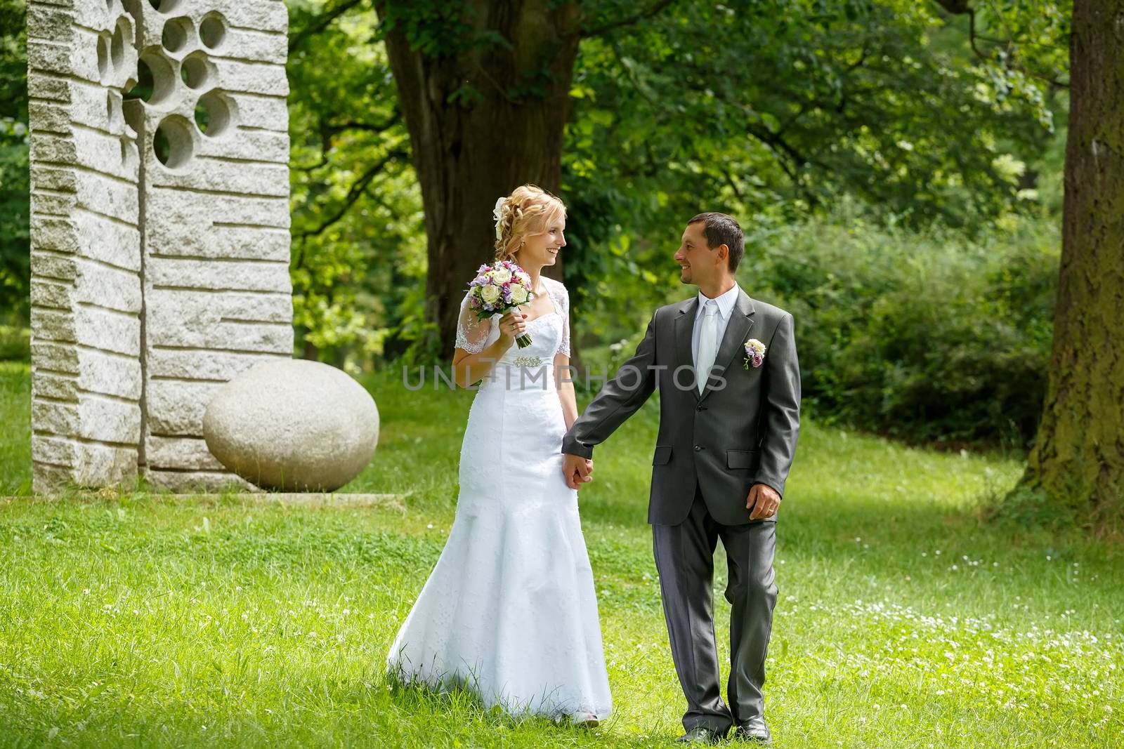 beautiful young wedding couple, blonde bride with flower and her groom in summer park