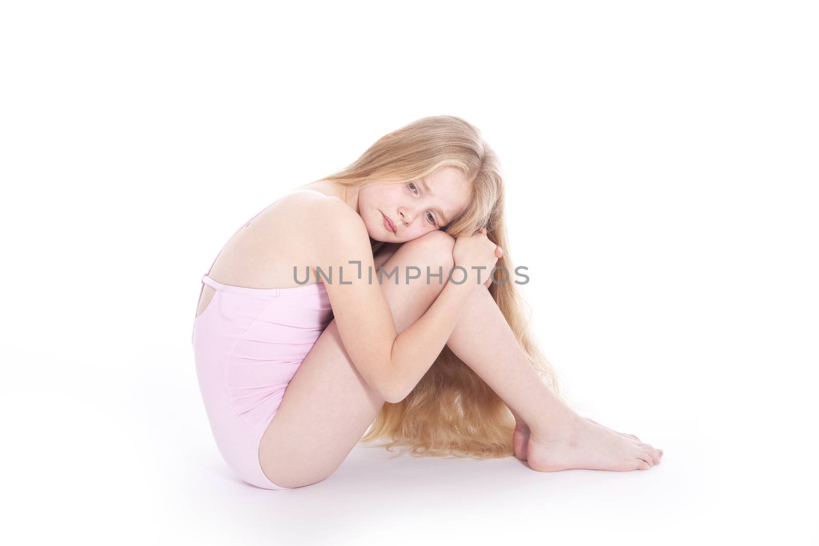 young girl in pink with sad expression sitting on floor of studio against white background