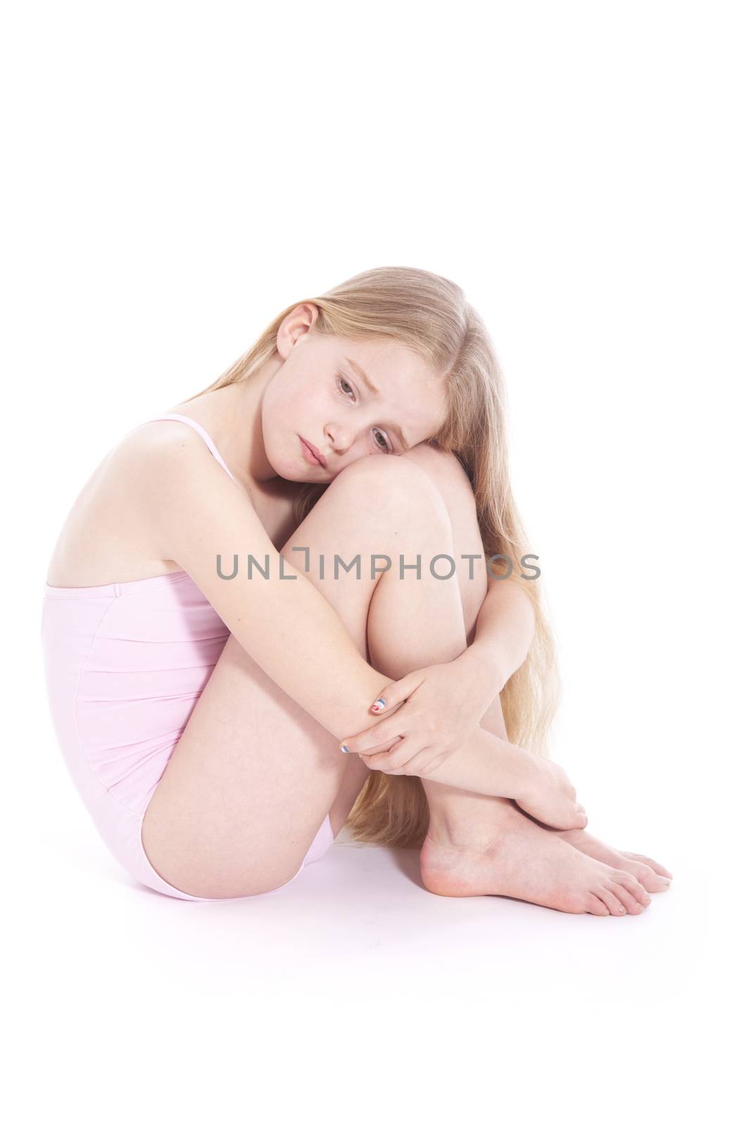 young girl in pink with sad expression sitting on floor of studio against white background