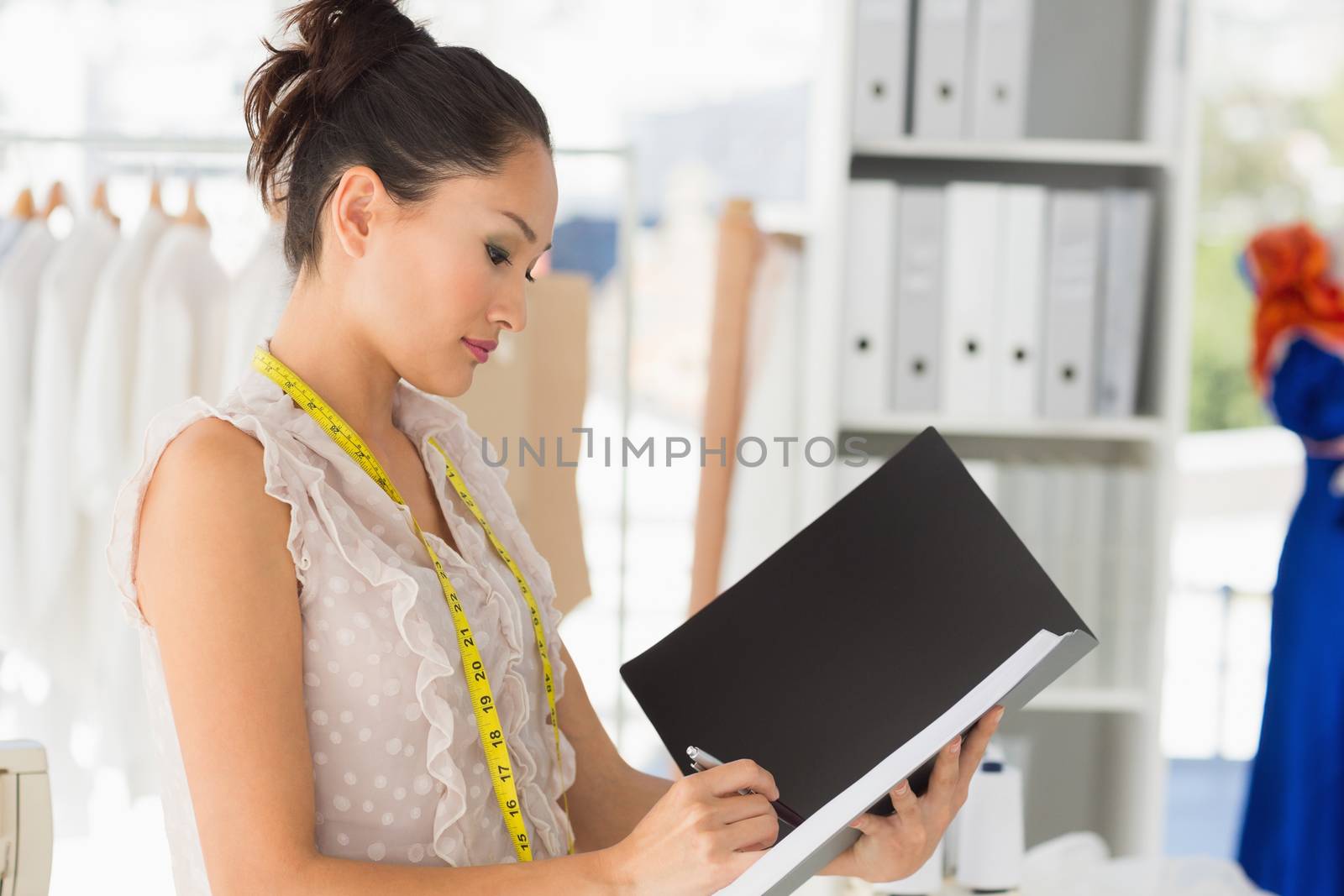Beautiful female fashion designer looking at folder in the studio