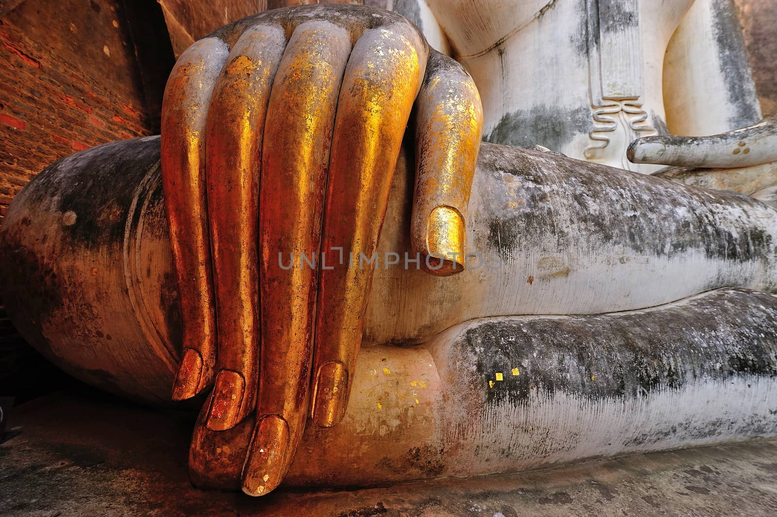 gold leaf offerings on slender fingers of wat si chums, Thailand by think4photop