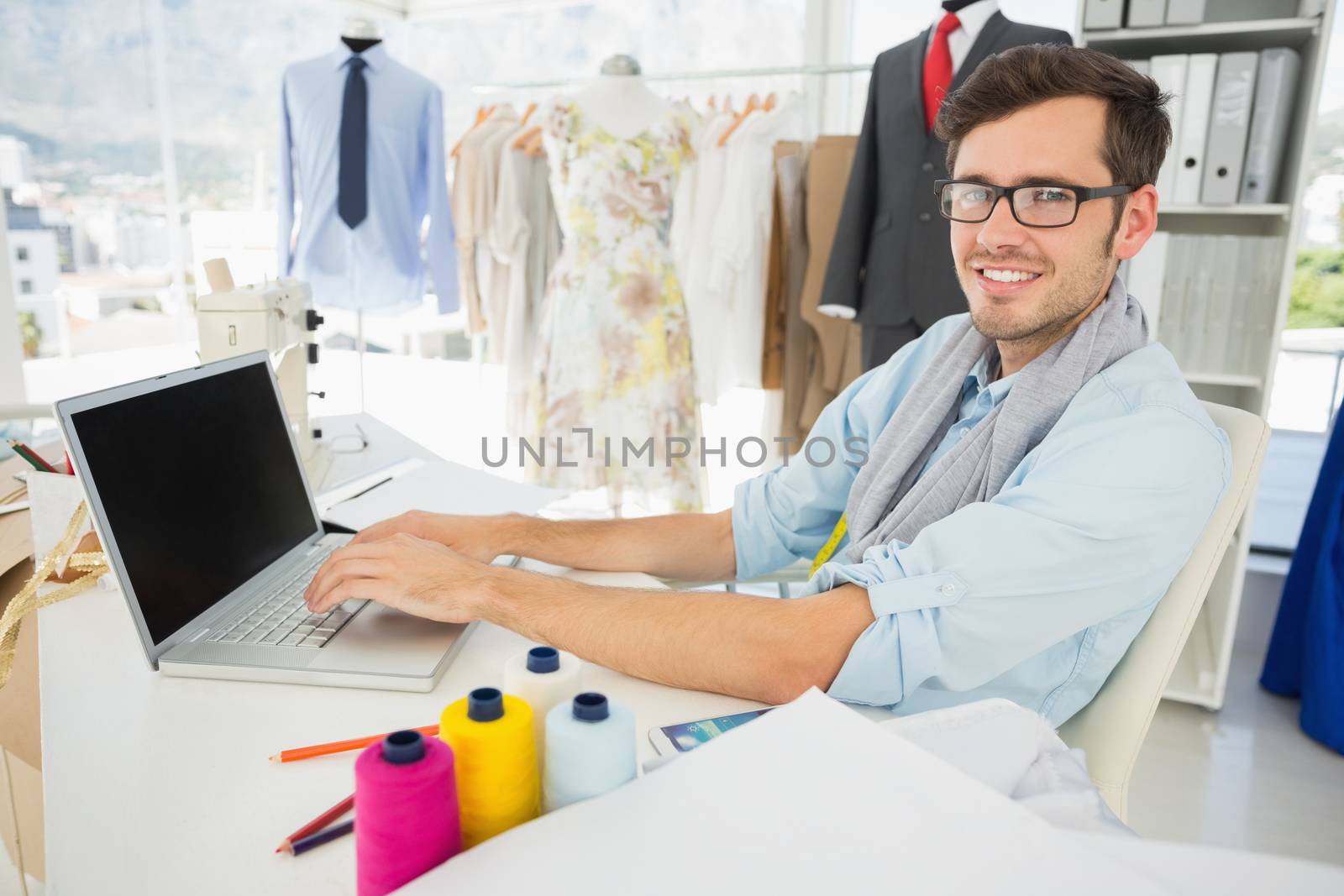 Side view portrait of a young male fashion designer using laptop in the studio