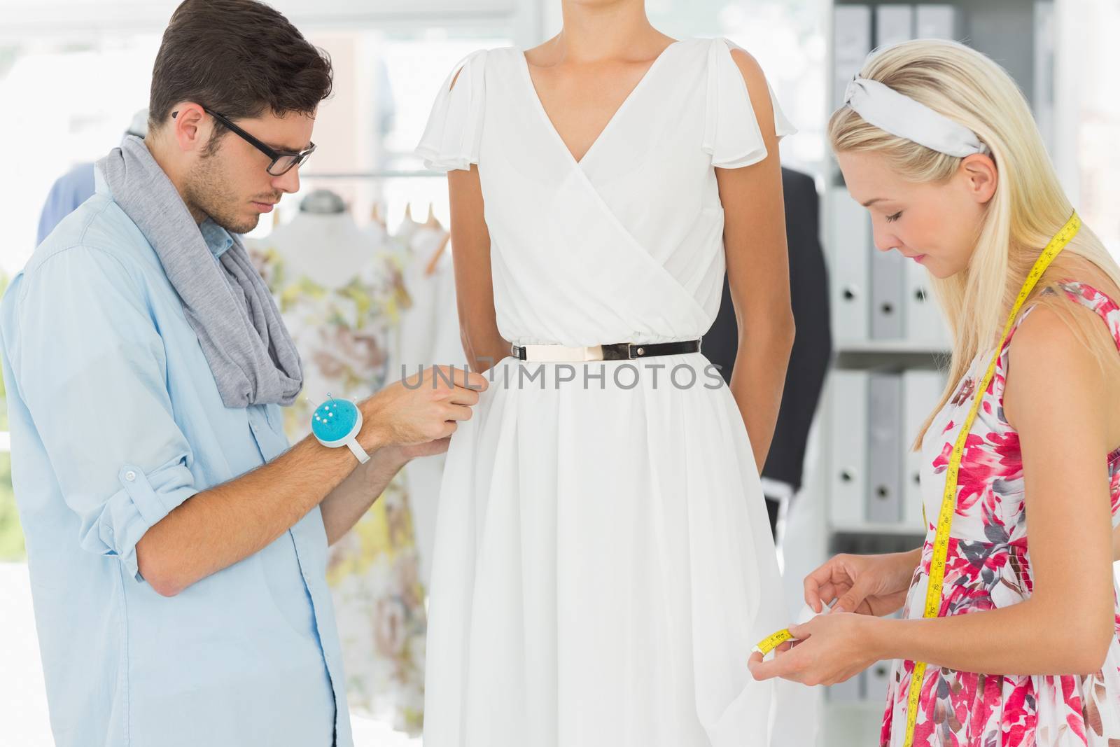 Two fashion designers adjusting dress on model in the studio