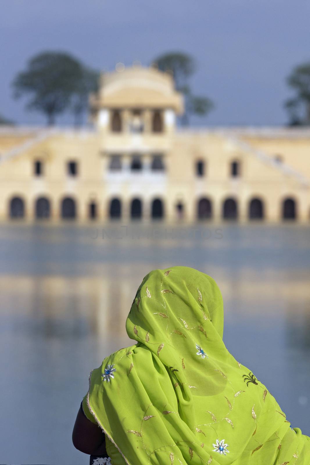 Indian lady in colorful sari looking out over the Water Palace (Jal Mahal) in the middle of Man Sagar lake. Jaipur, Rajasthan, India. 18th Century