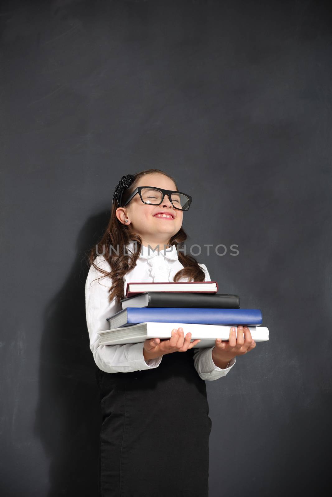 Schoolgirl holding heavy books standing on a background of black wall by robert_przybysz