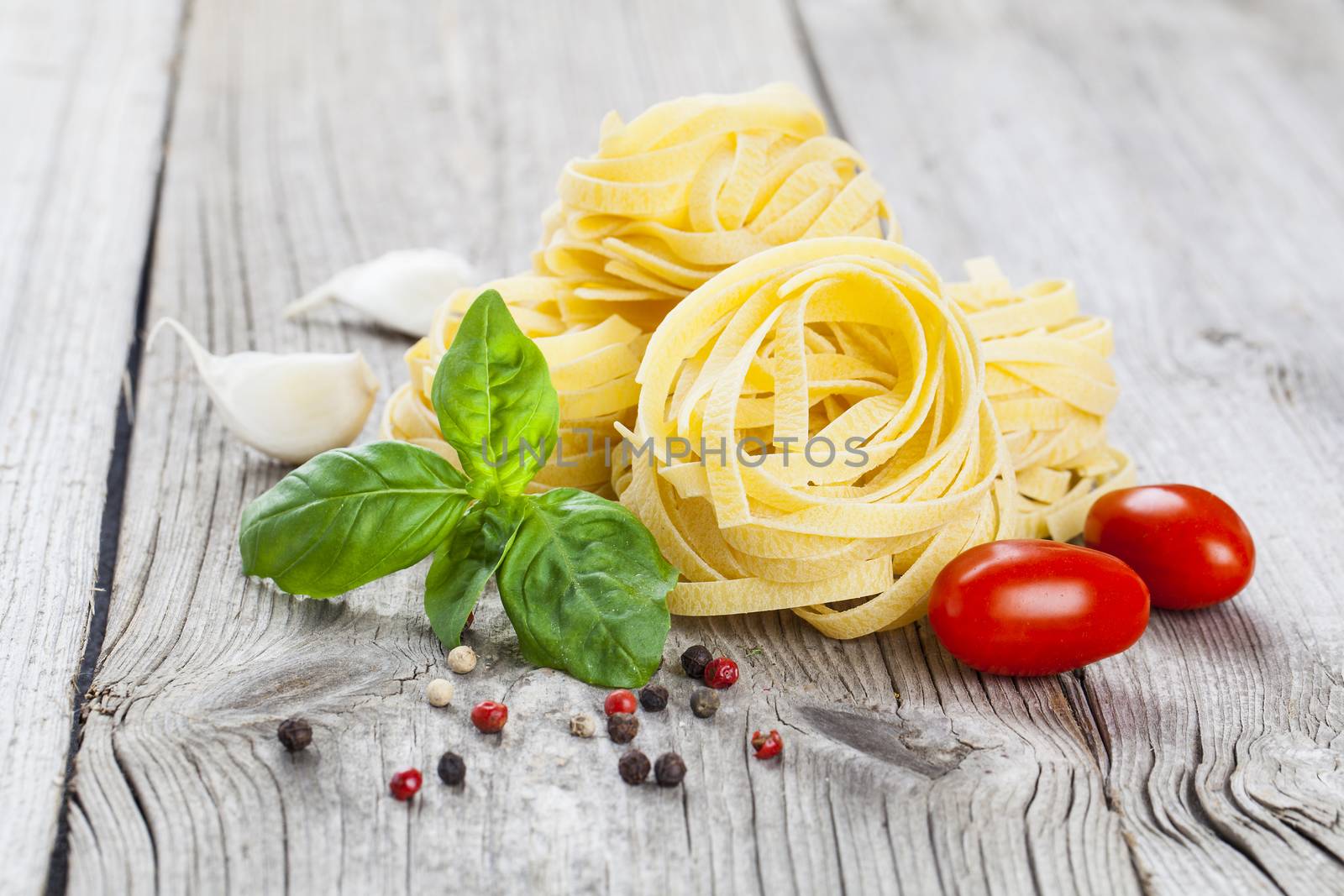 Italian pasta fettuccine nest with garlic, tomatoes and fresh basil leaves, on wooden background