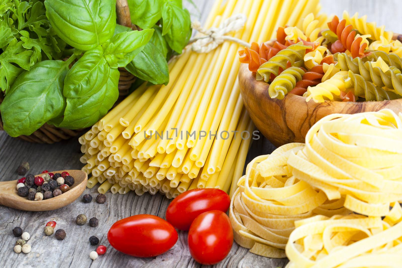 Italian pasta, spaghetti, fettuccine nest with garlic, tomatoes and fresh basil leaves, on wooden background