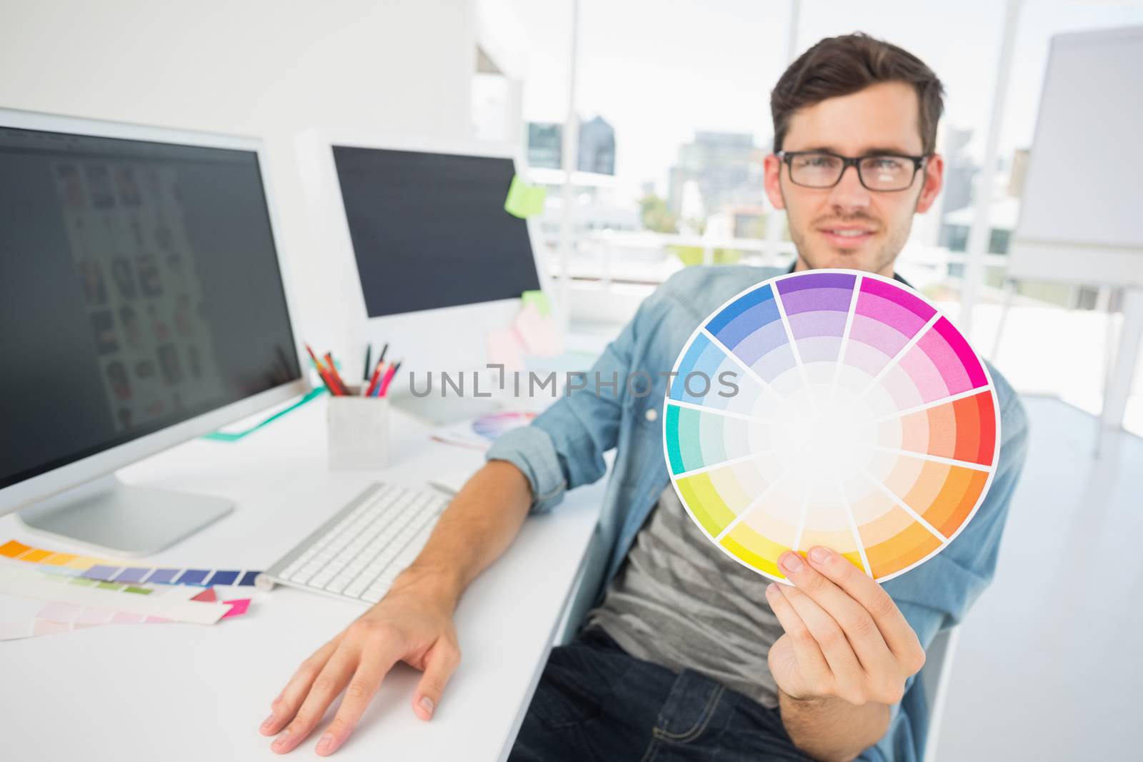 Portrait of a male artist holding color wheel by computer at desk