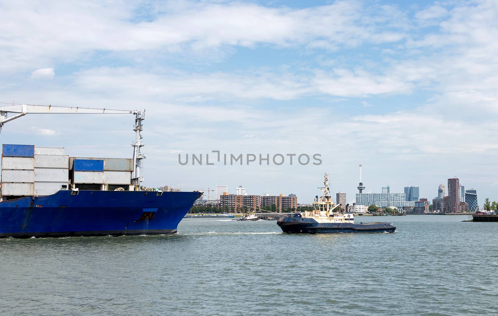 containership entering rotterdam harbor with tug and skyline as background