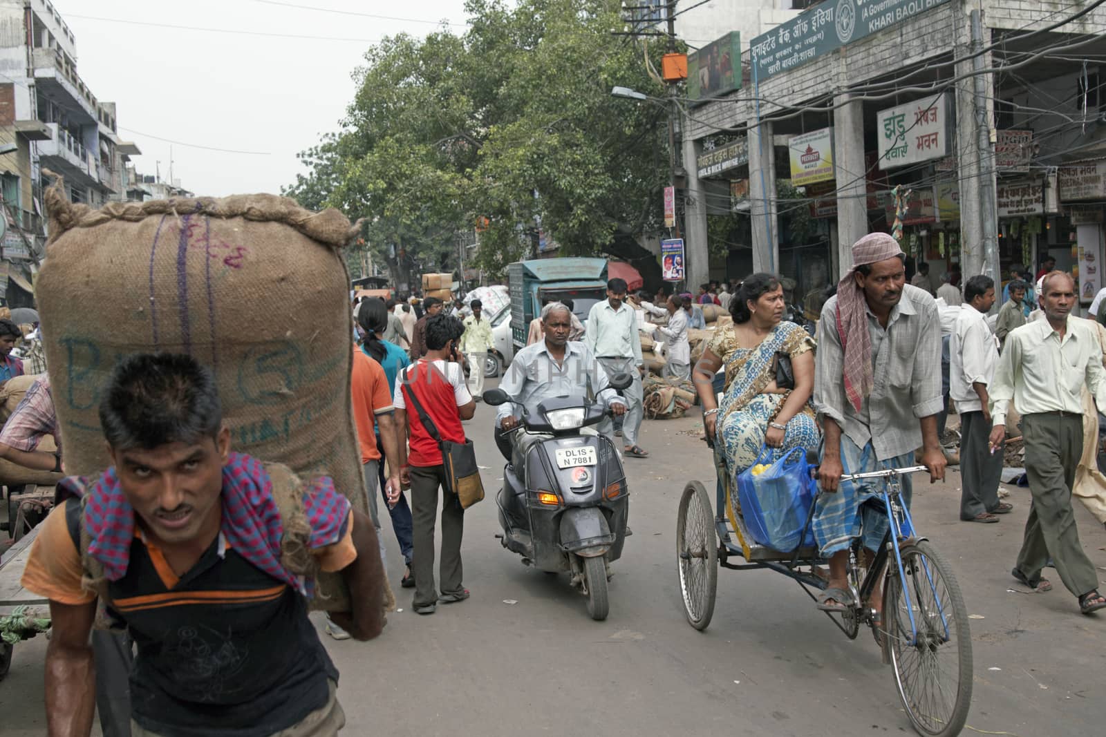 Man carrying heavy sack along crowded street in Old Delhi, India.