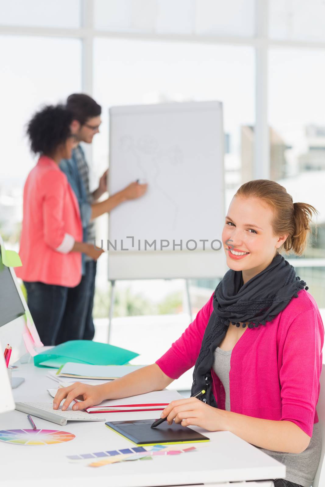 Portrait of a female artist using graphic tablet with colleagues behind at the office