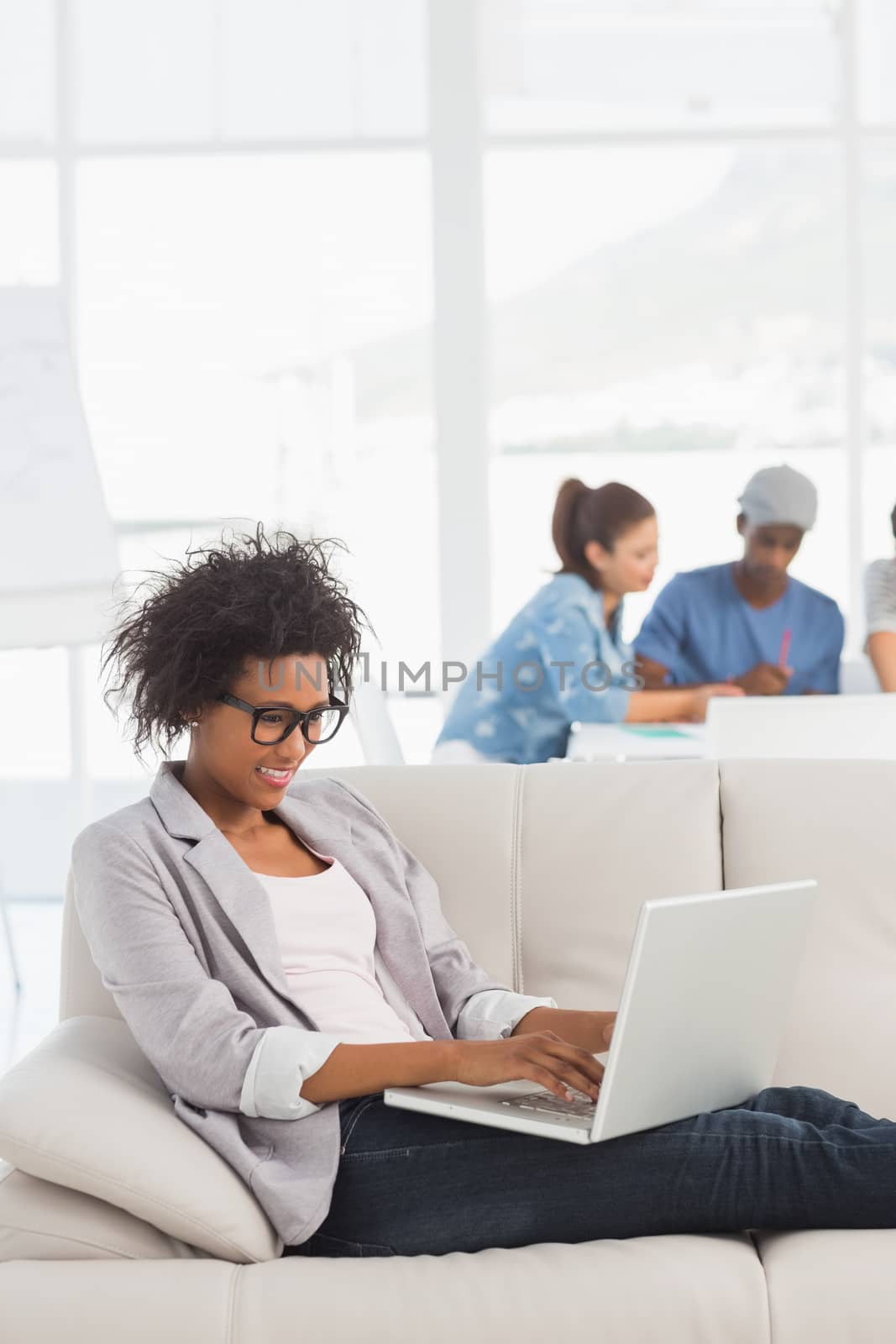 Young woman using laptop with colleagues in background at a creative bright office