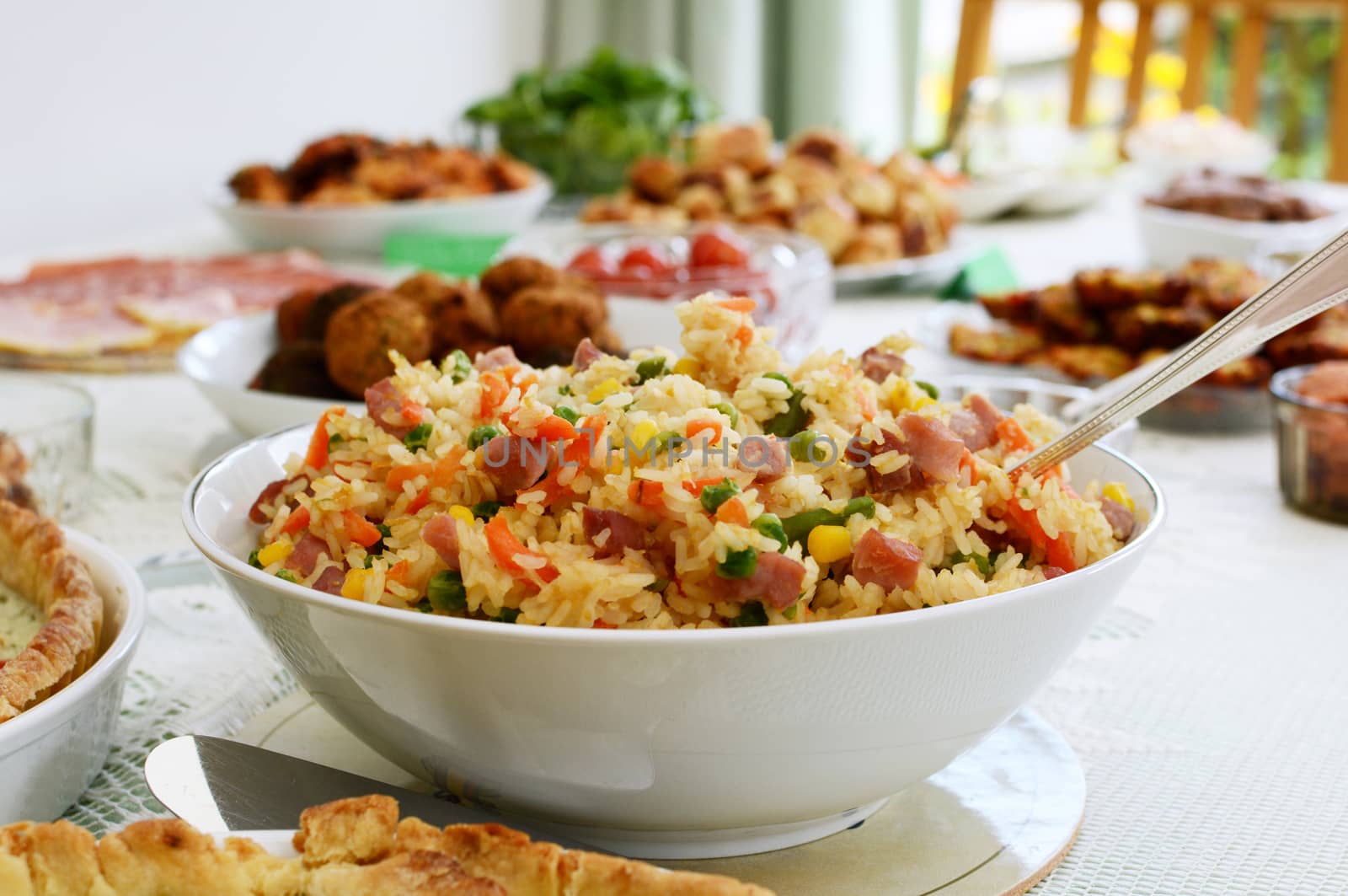 Bowl of gammon and mixed vegetable rice salad with other party food on a buffet table