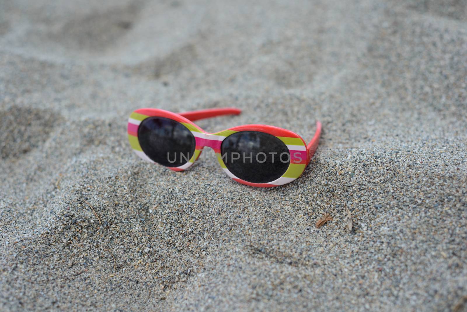 Used children's striped sunglasses lying on the sand