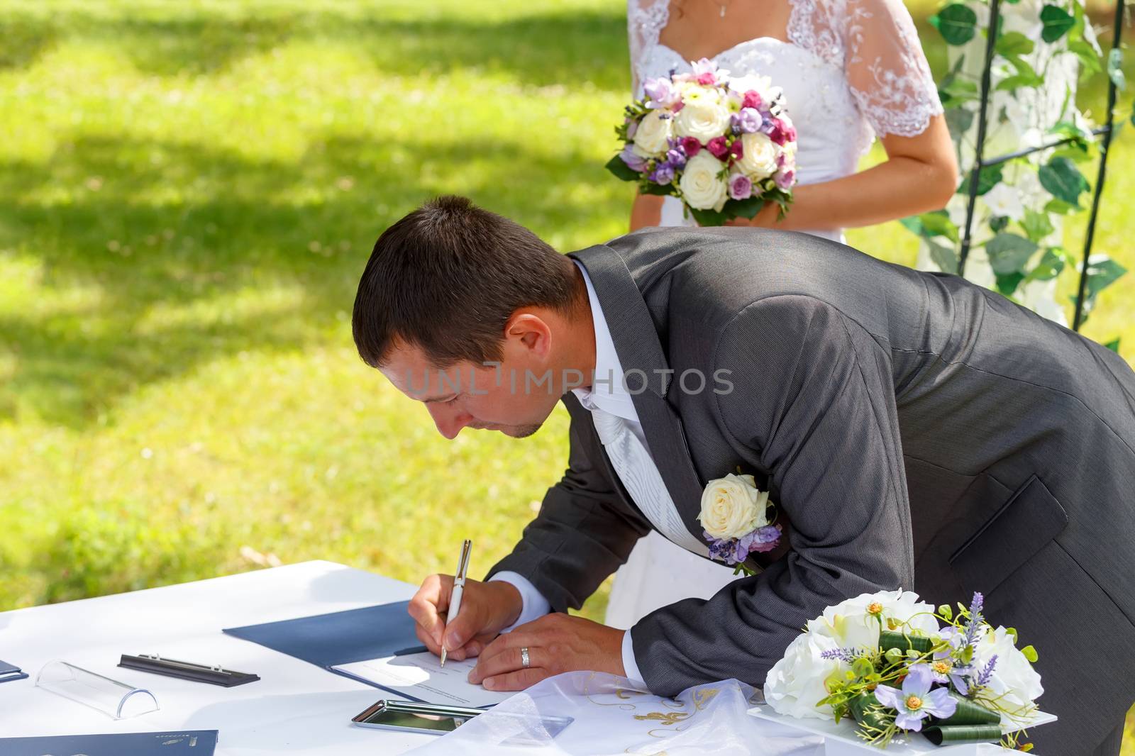 groom signing wedding certificate in park with bride in background
