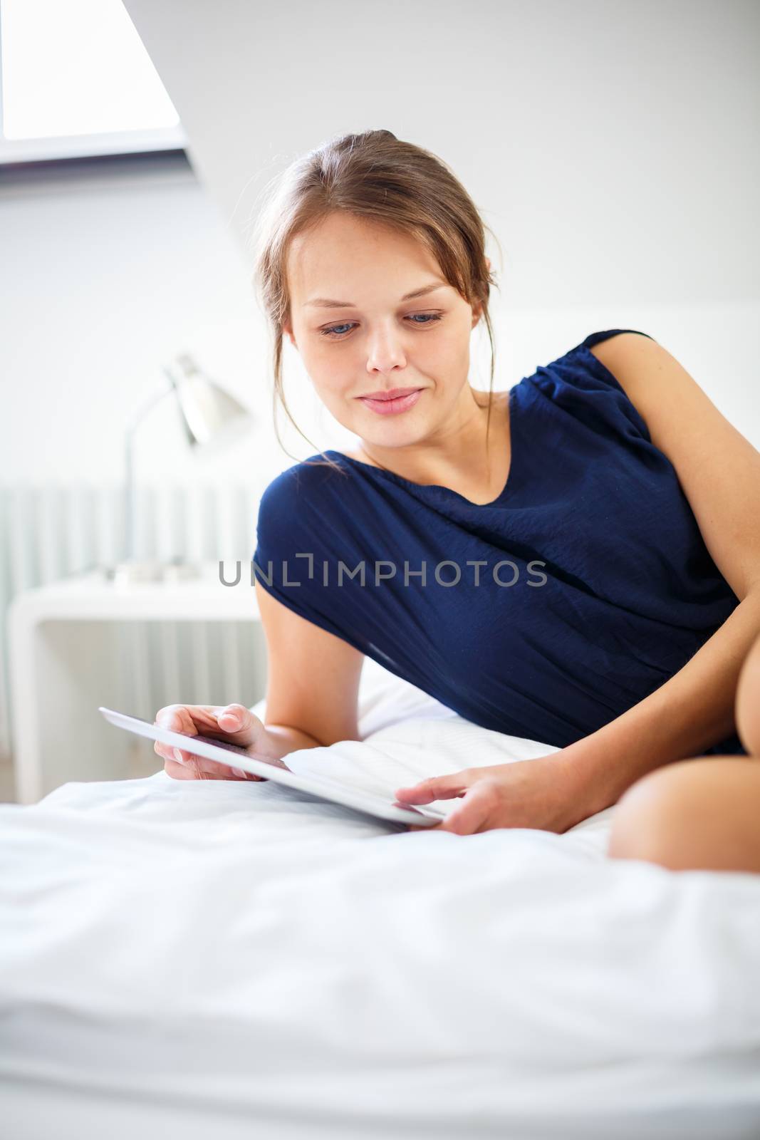 Elegant, smart, young woman using her tablet computer in bed by viktor_cap