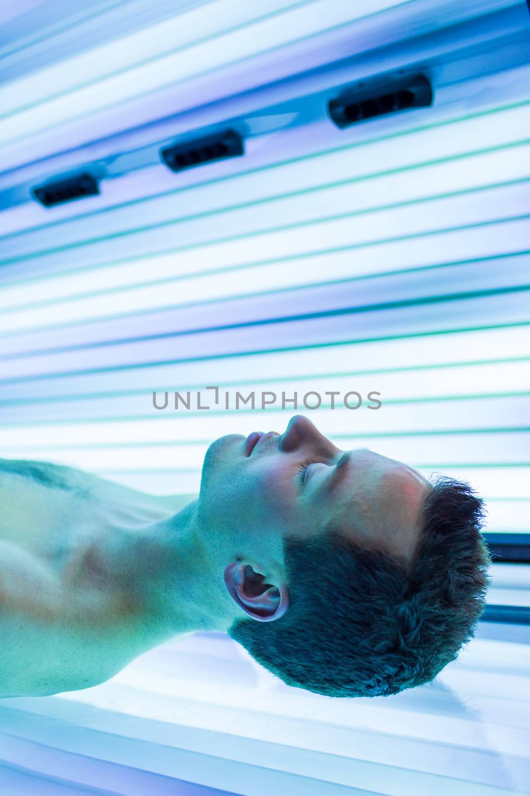 Handsome young man relaxing during a tanning session in a modern by viktor_cap