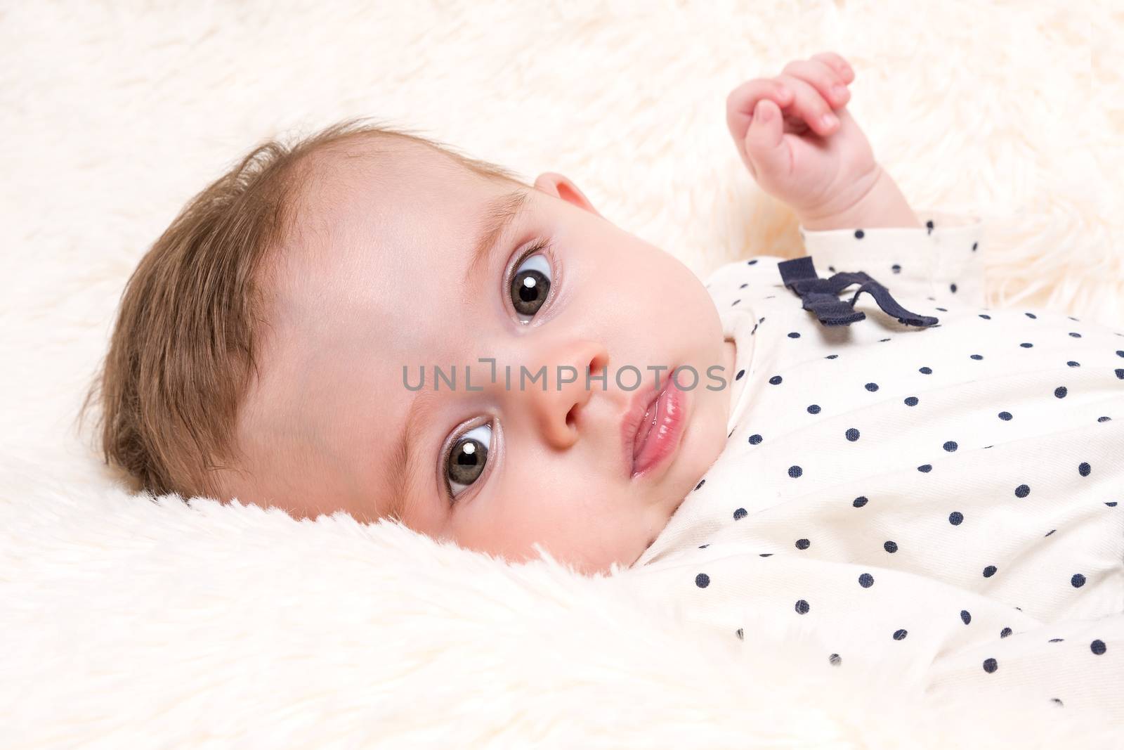 Portrait of Beautiful Baby Girl in Spotty Top resting on Cream Fur Rug