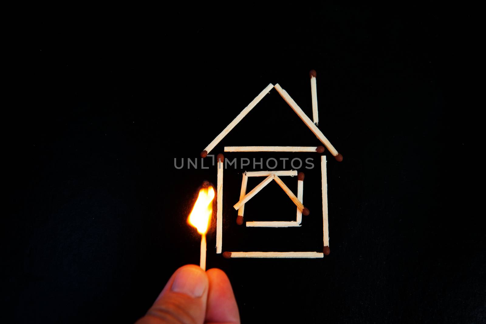 burning match in hand near the model of the house