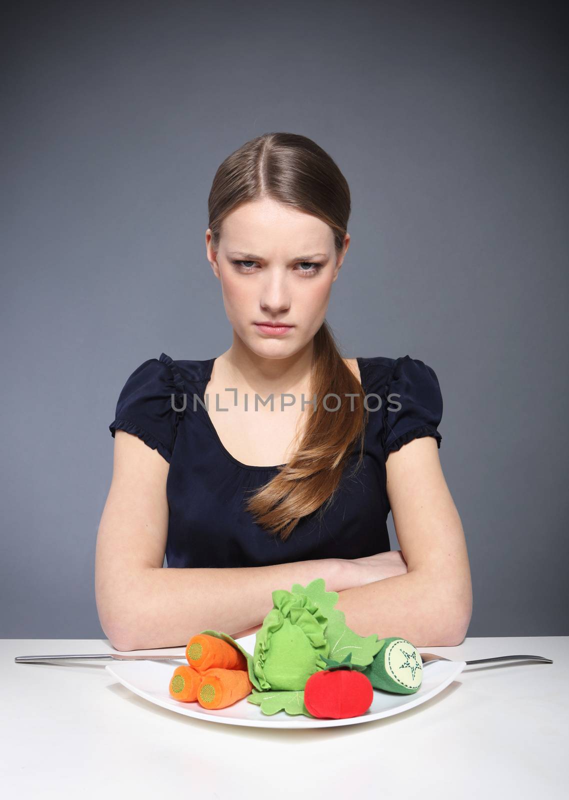 Young girl sitting over a plate of vegetables and put into the mouth barbed wire.