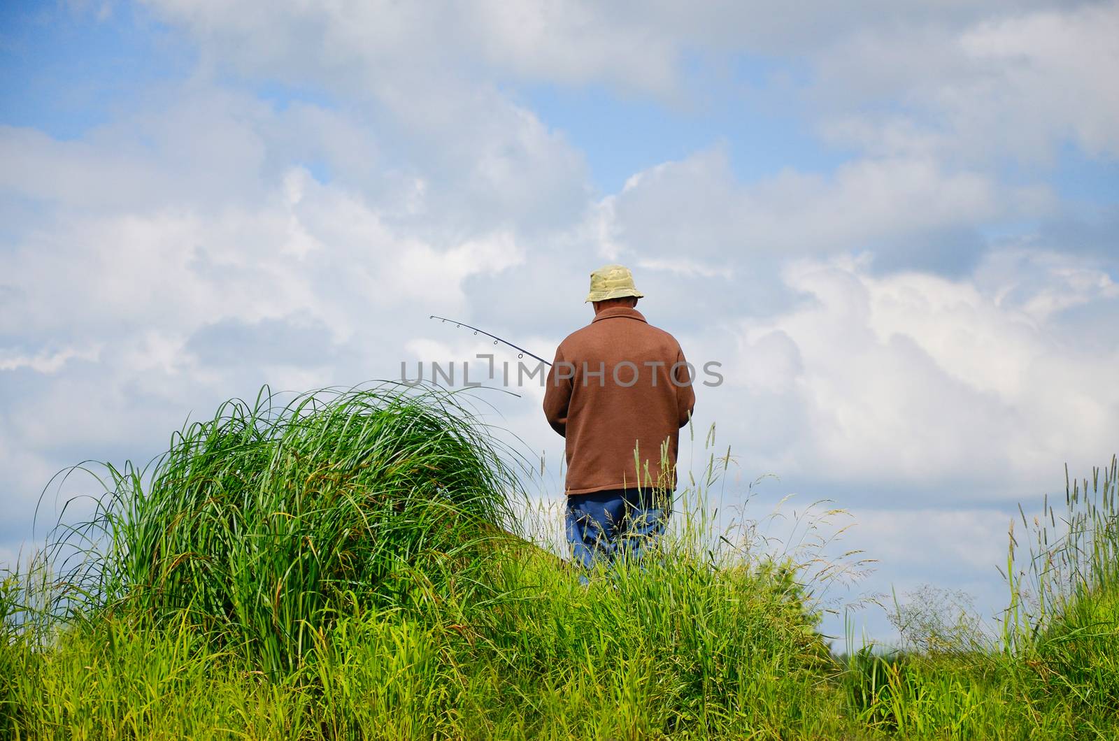 Fisherman in anticipation of catch with a fishing rod on the waterfront on the background of blue sky with clouds