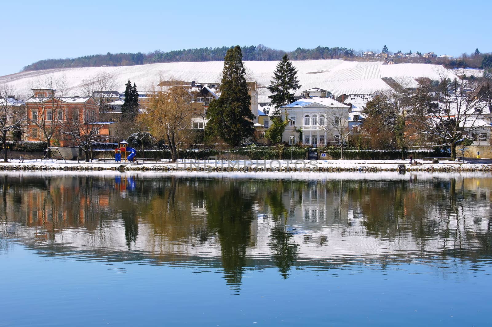 Bernkastel Kues in winter, trees and houses are reflected in the calm waters of the Moselle