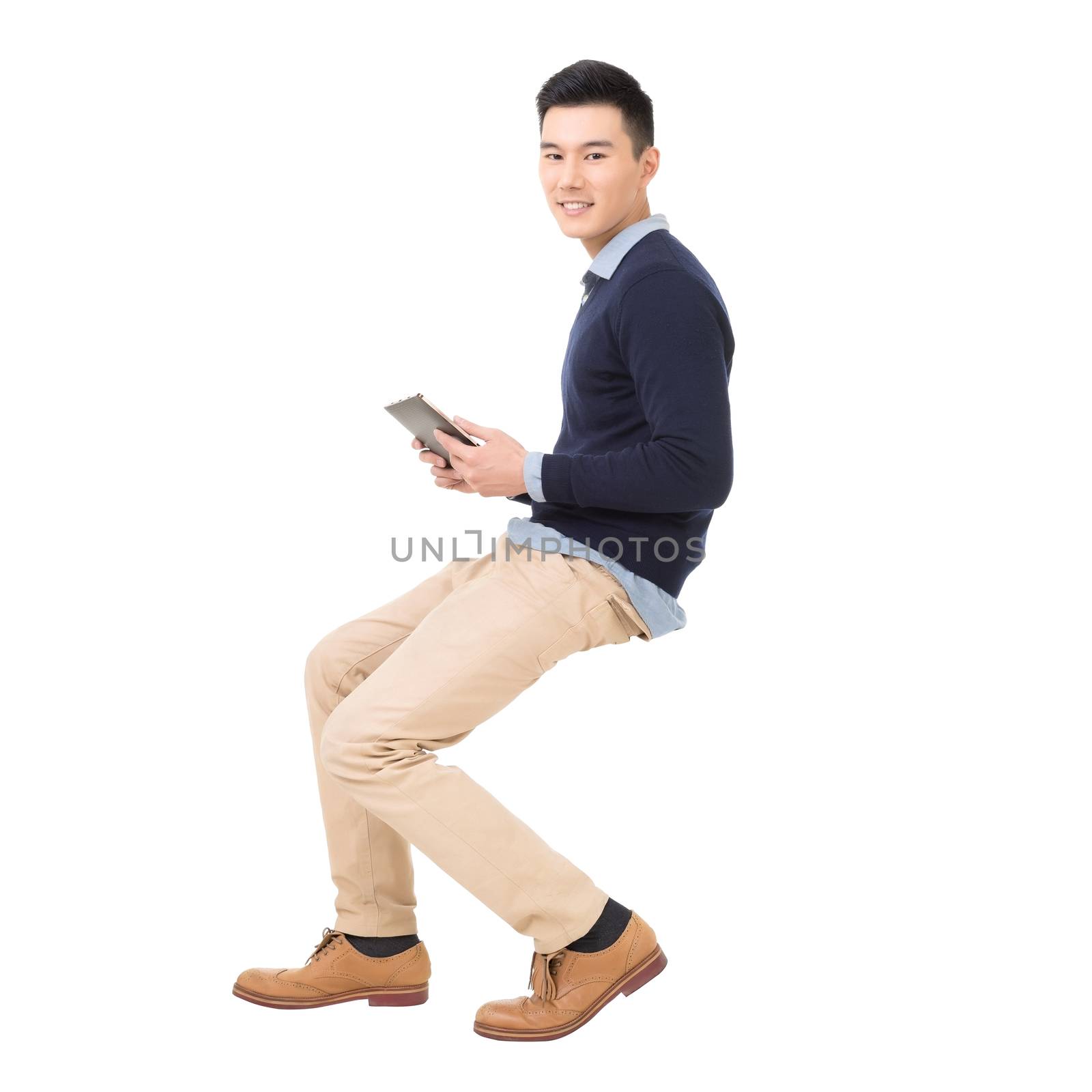 Handsome Asian guy sit and use pad, full length portrait isolated on white background.