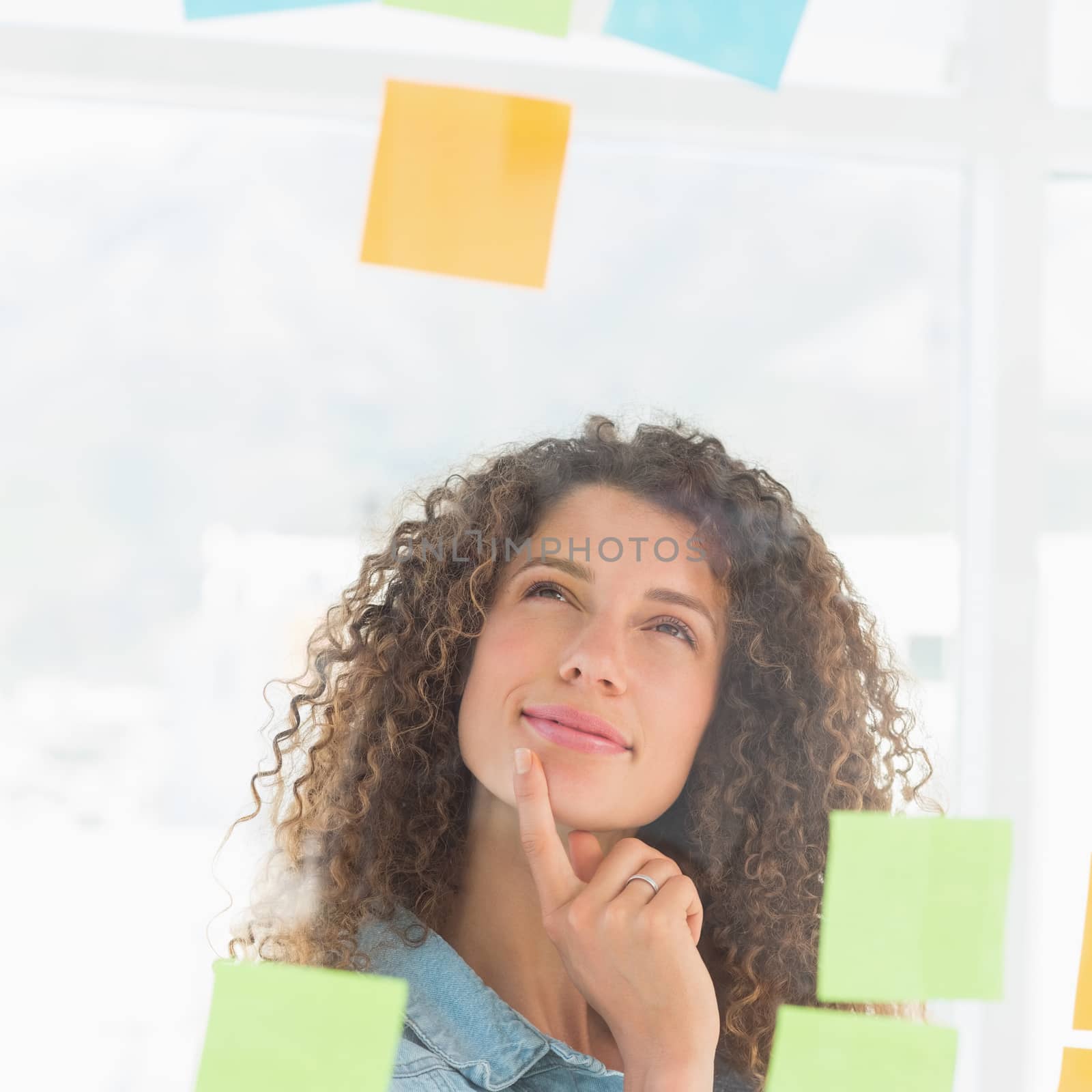 Thinking smiling designer looking at sticky notes on window in creative office