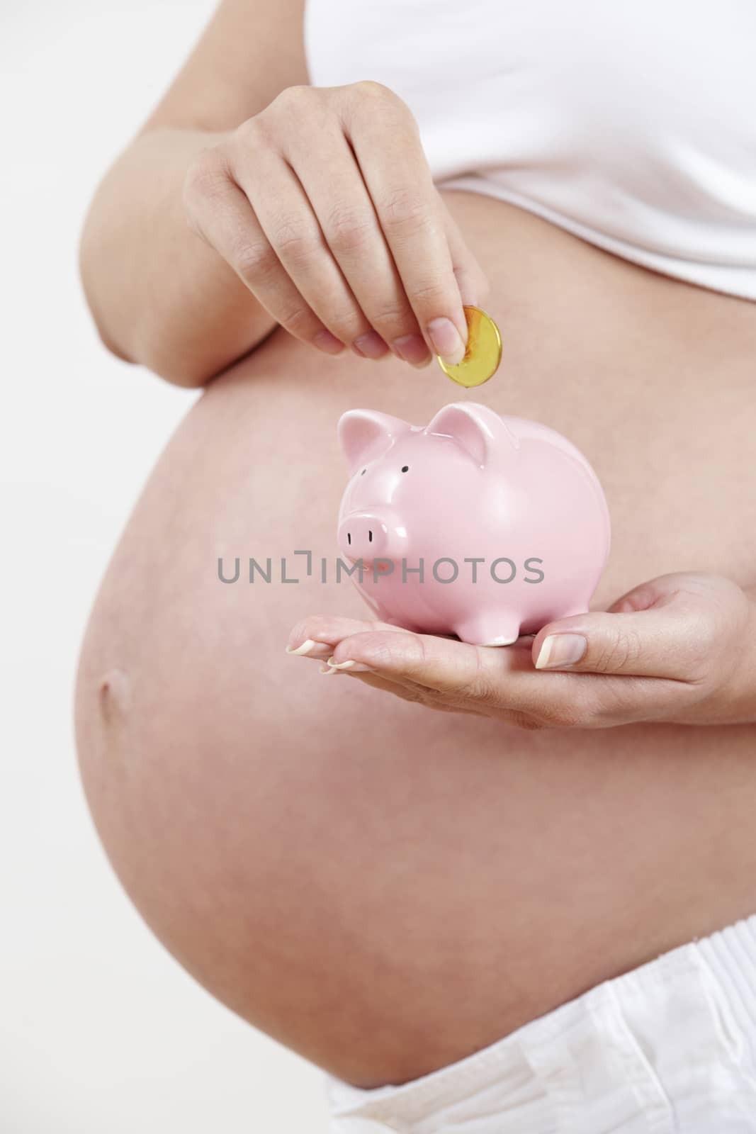 Close Up Of Pregnant Woman Putting Coin Into Piggy Bank