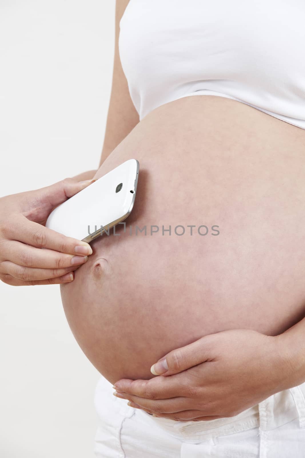 Close Up Of Pregnant Woman Holding Mobile Phone To Bump