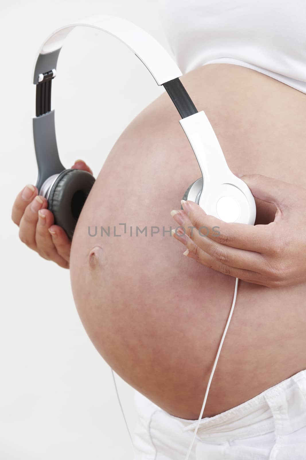 Close Up Of Pregnant Woman Holding Headphones Over Belly by HighwayStarz