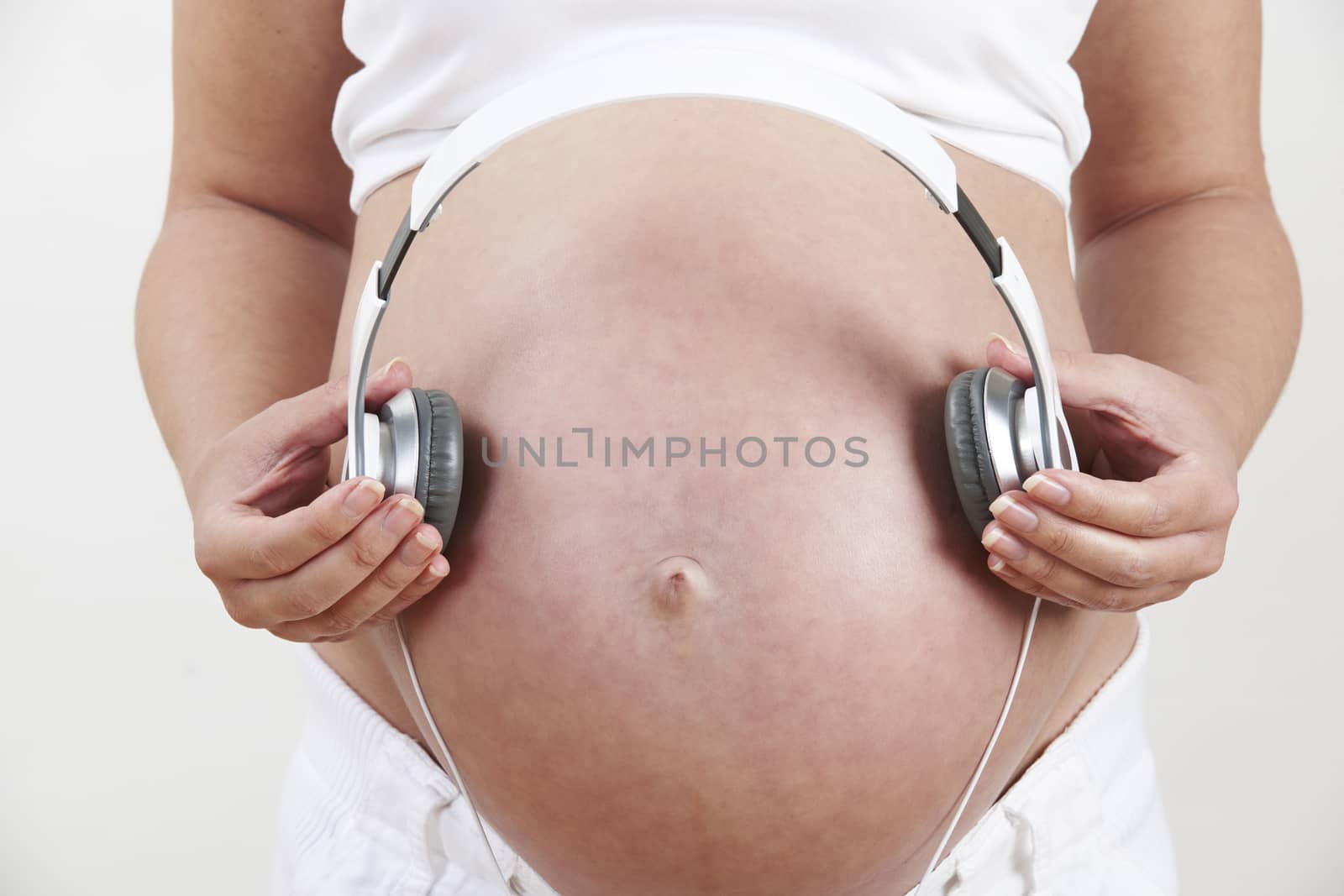 Close Up Of Pregnant Woman Holding Headphones Over Belly by HighwayStarz