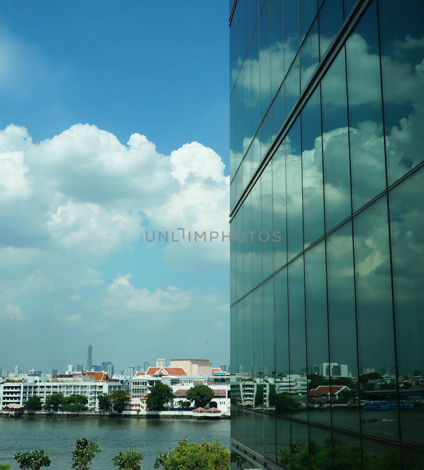 Tall buildings with modern style creating a mirror, reflecting the light from outside the building, reflecting  the clouds that floating by and the beautiful of blue sky.                               