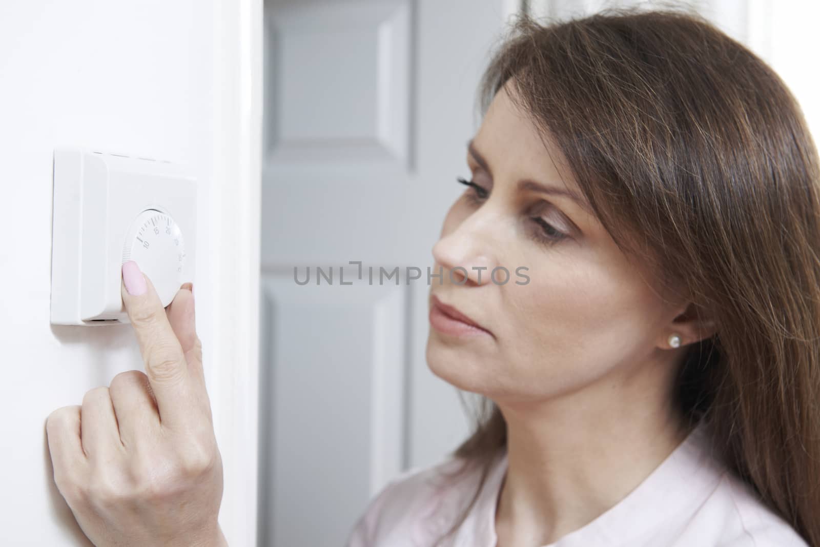 Woman Adjusting Thermostat On Central Heating Control