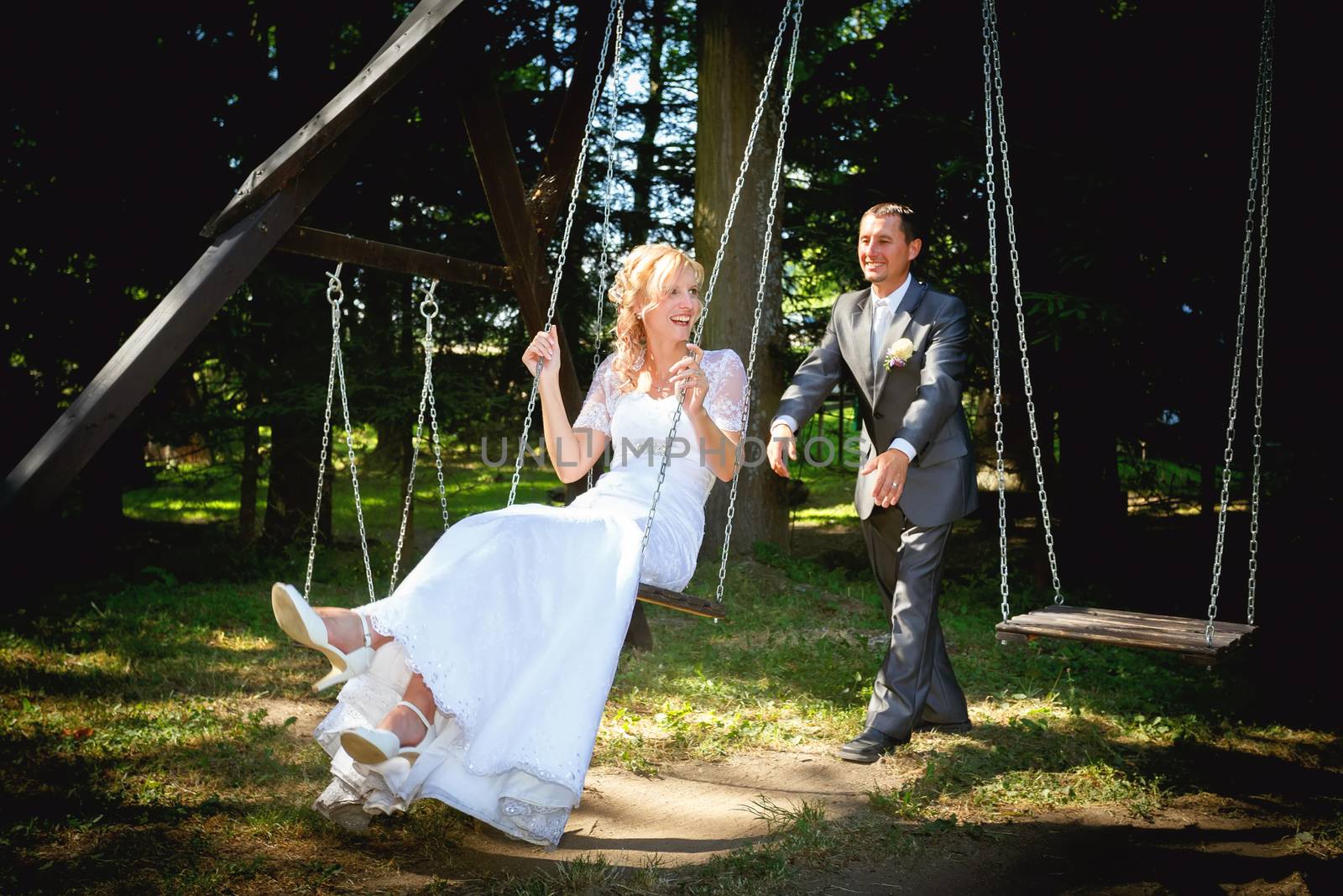 beautiful young wedding couple in park, blonde bride on swing and her groom