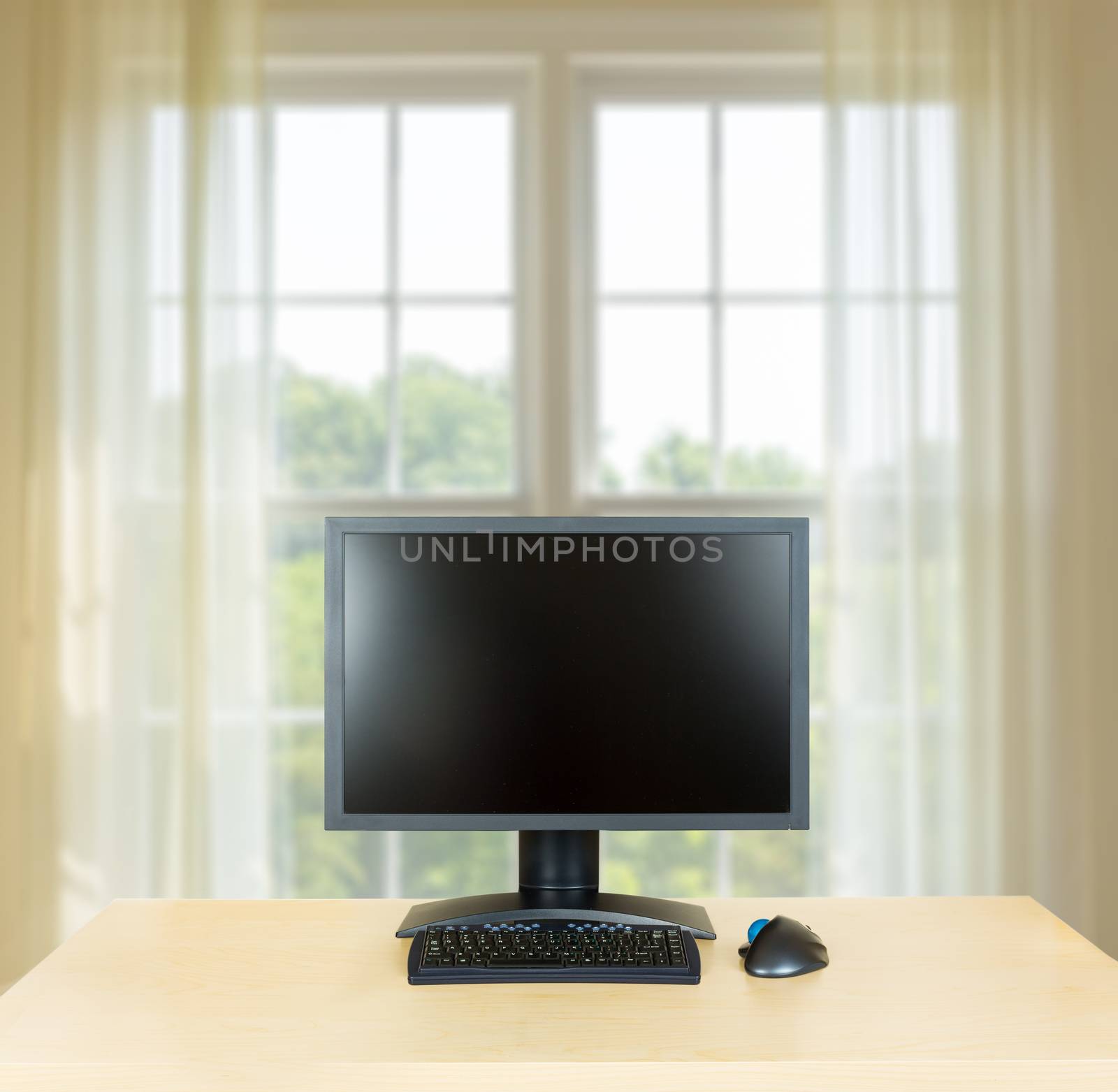 Plain light colored wooden desk with computer monitor and keyboard to suggest calm, organization and meditation at work or in home office. Bright window in background