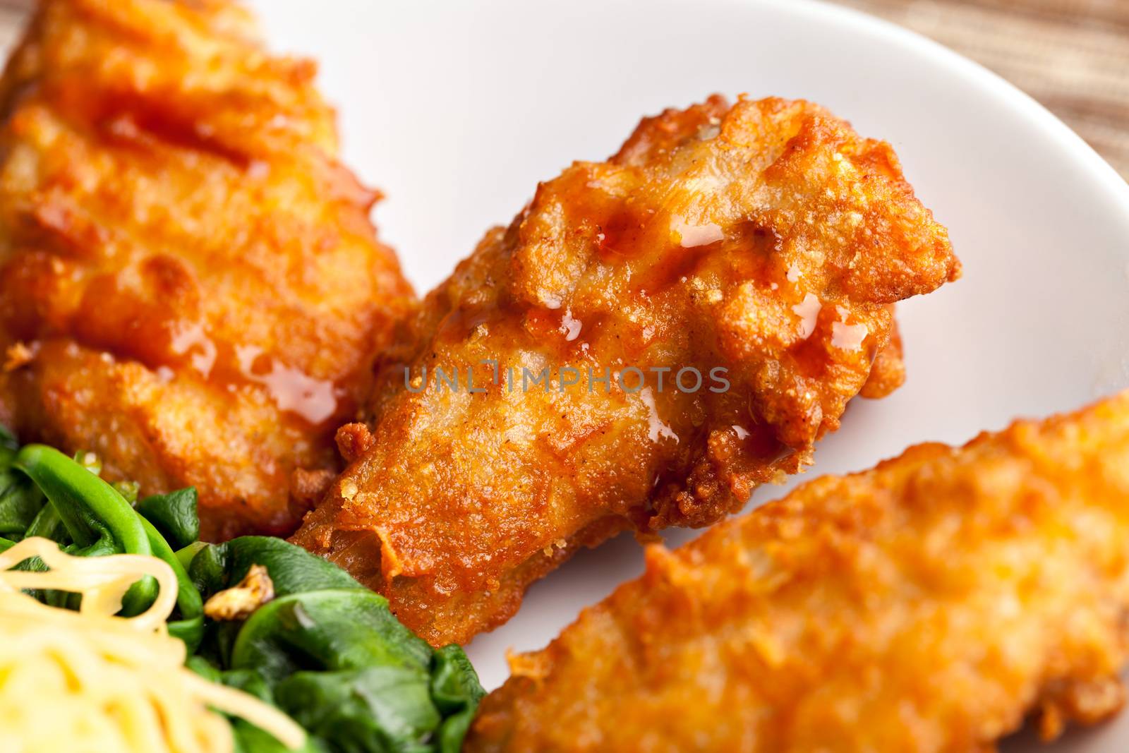 Thai style fried chicken wings on a round white plate with egg noodles and spinach. Close up with shallow depth of field.