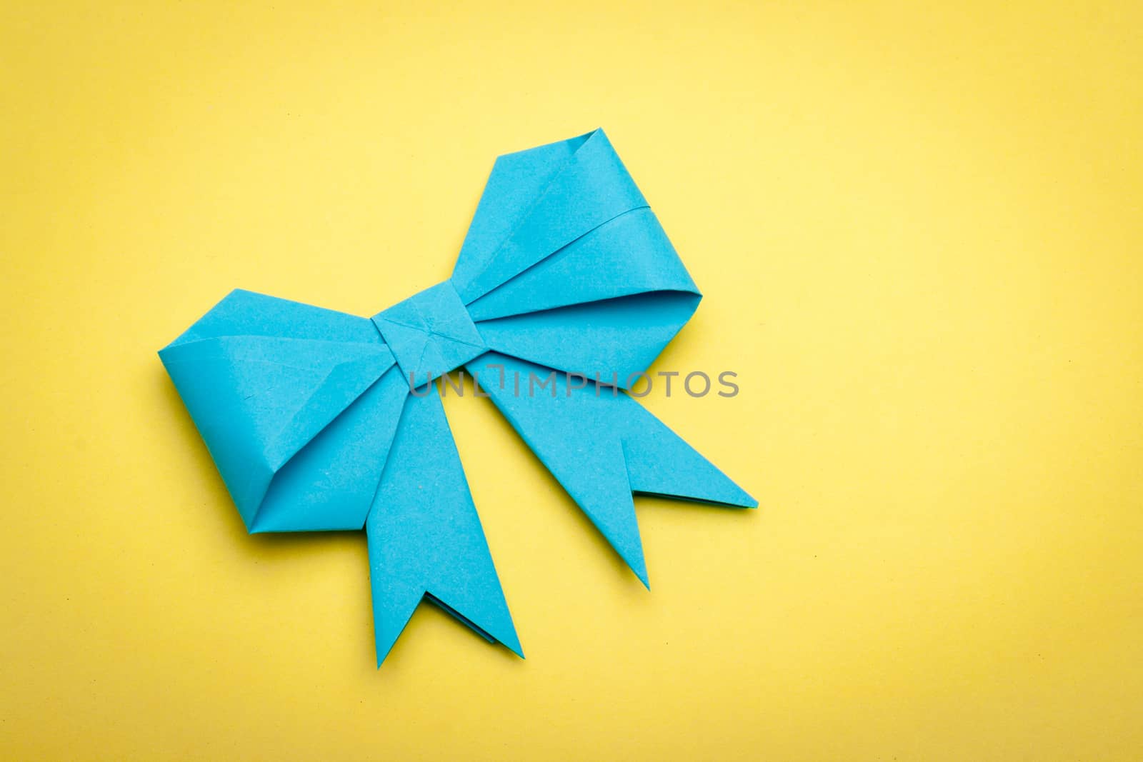 blue origami paper bow on yellow paper background