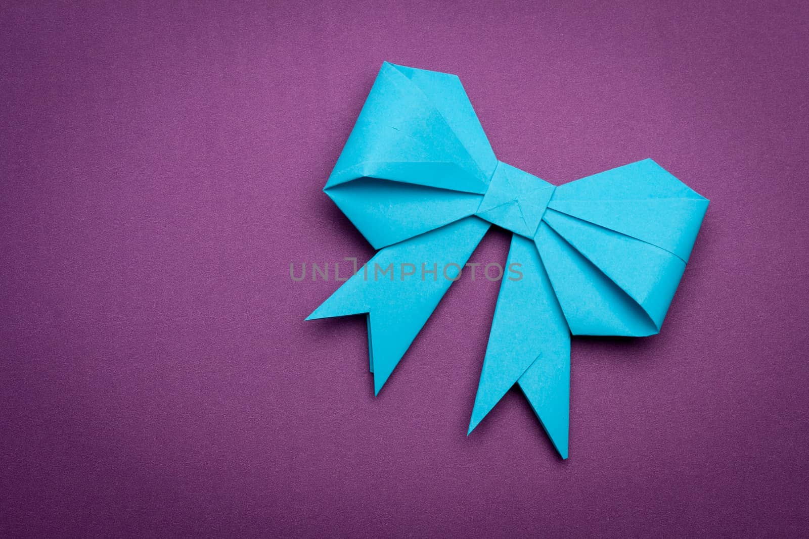 blue origami paper bow on purple paper background
