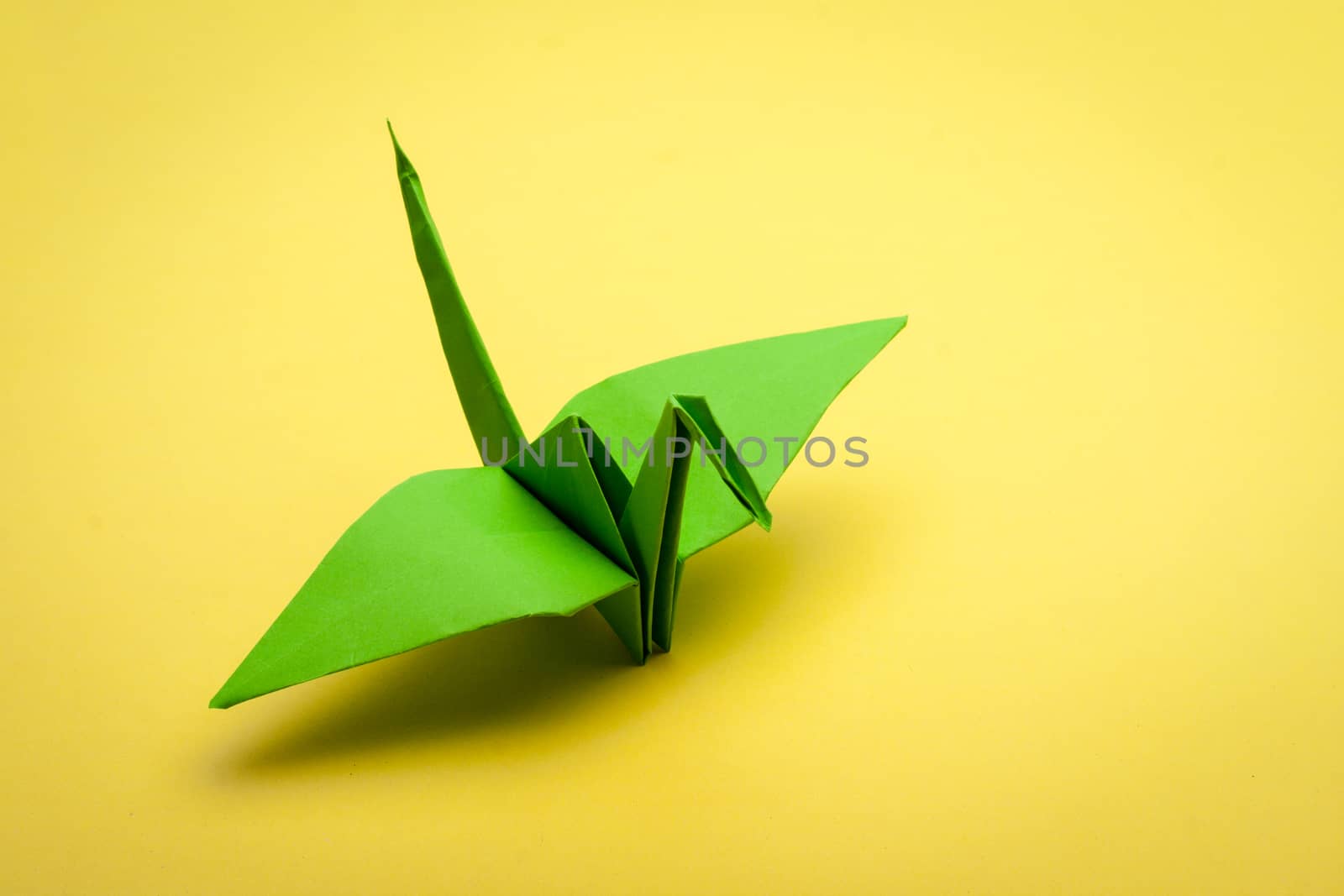 green origami paper crane on yellow paper background
