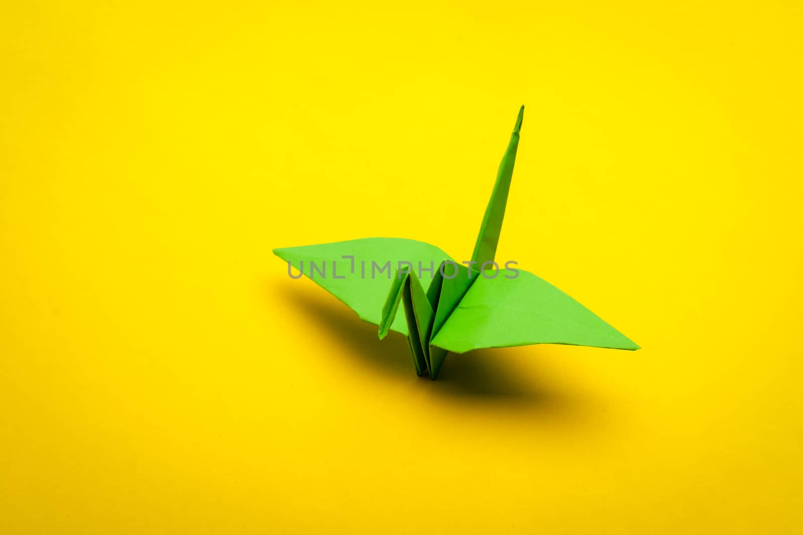 green origami paper crane on yellow paper background