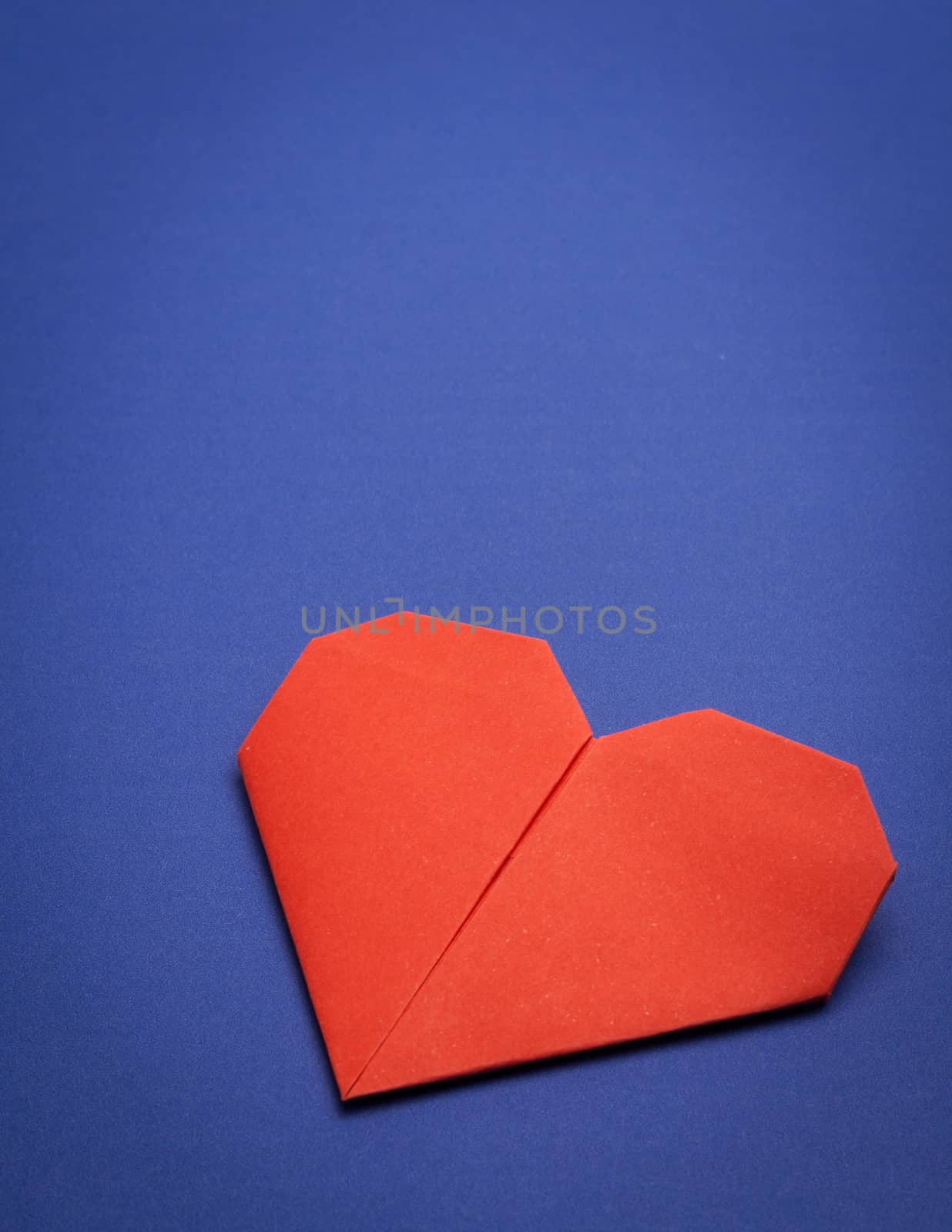 red origami paper heart on blue paper background